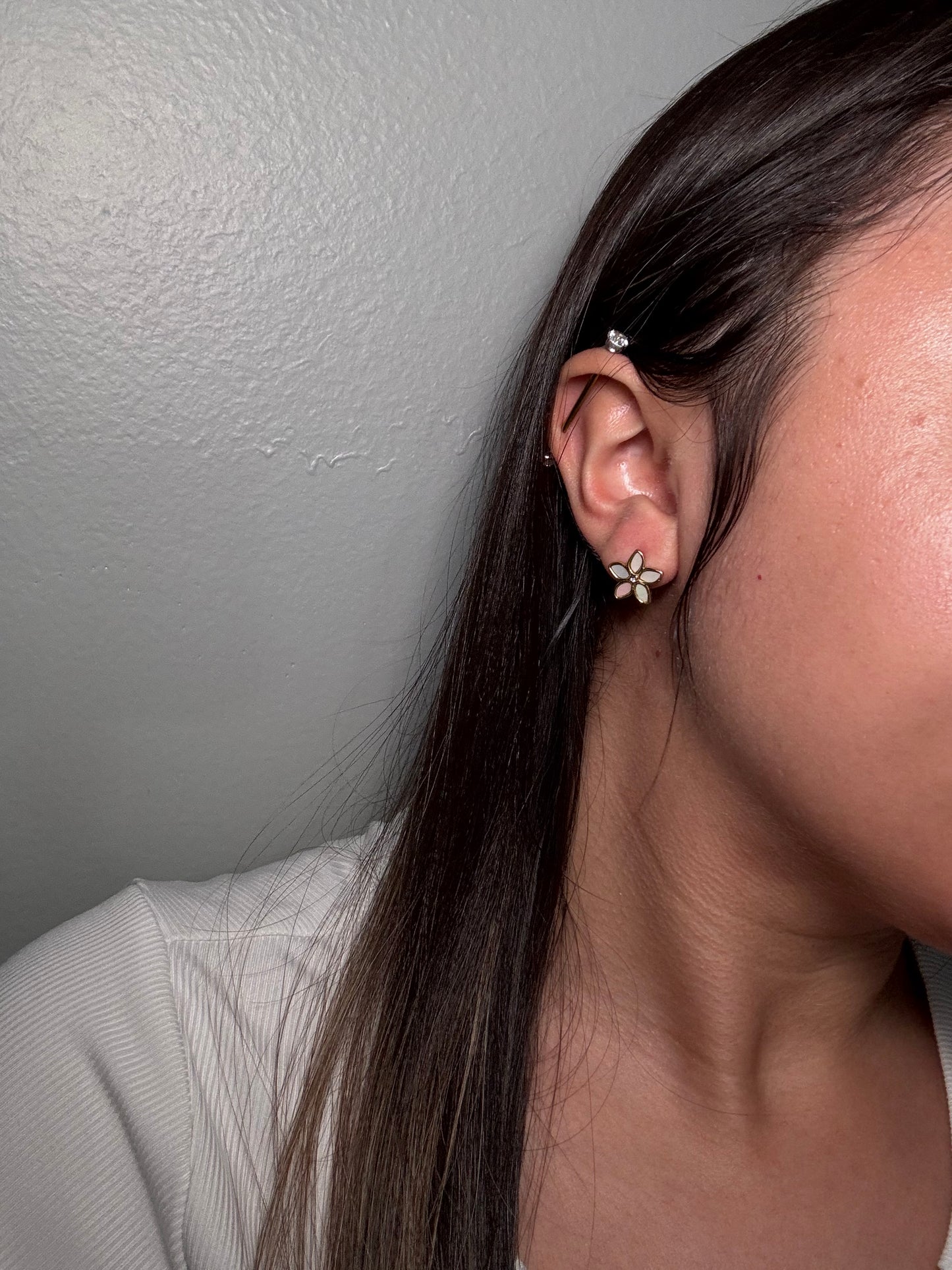 The Opalina floral stud earrings worn by model close-up on ear showing gold and enamel flower detail.