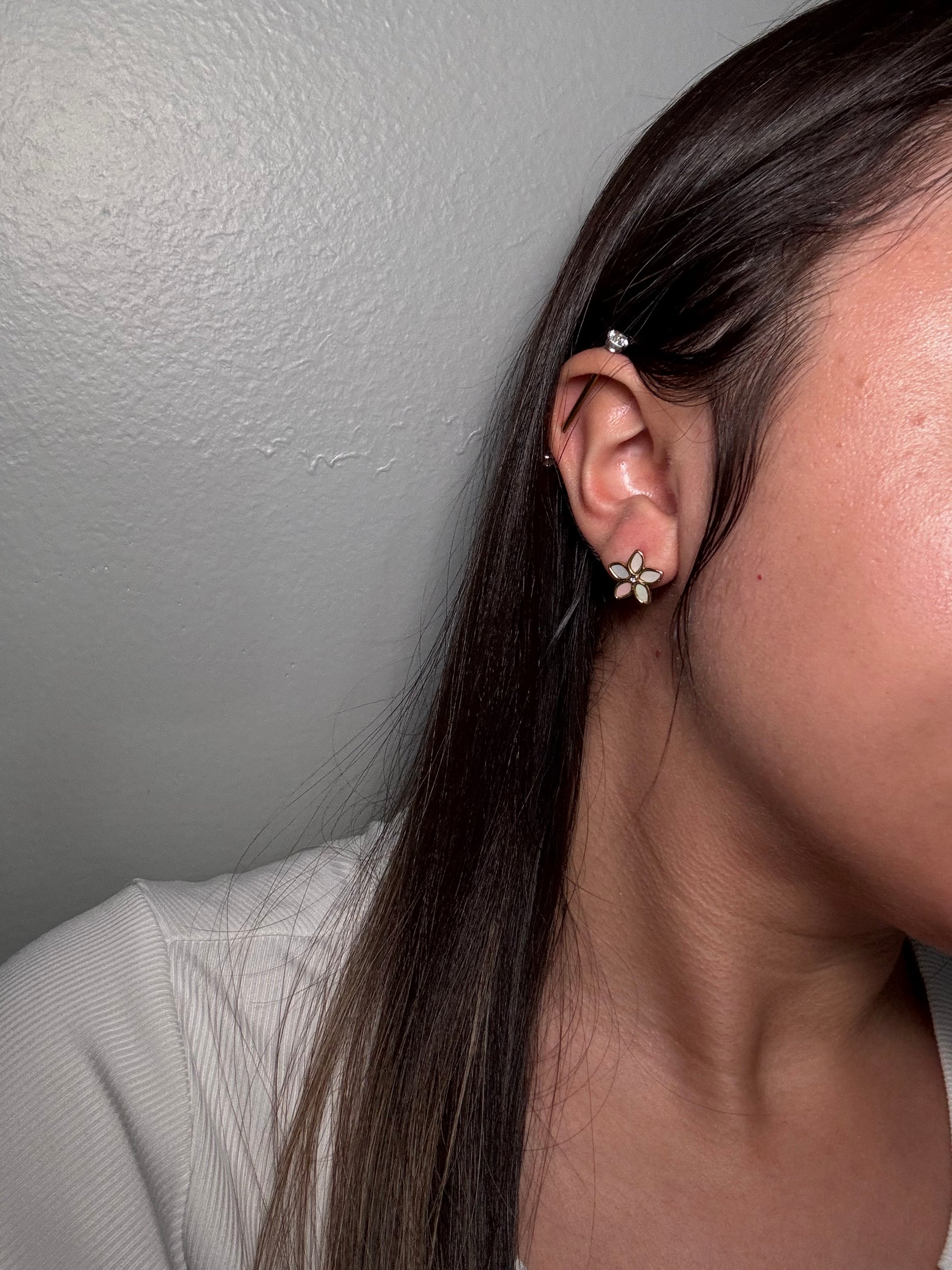 The Opalina floral stud earrings worn by model close-up on ear showing gold and enamel flower detail.