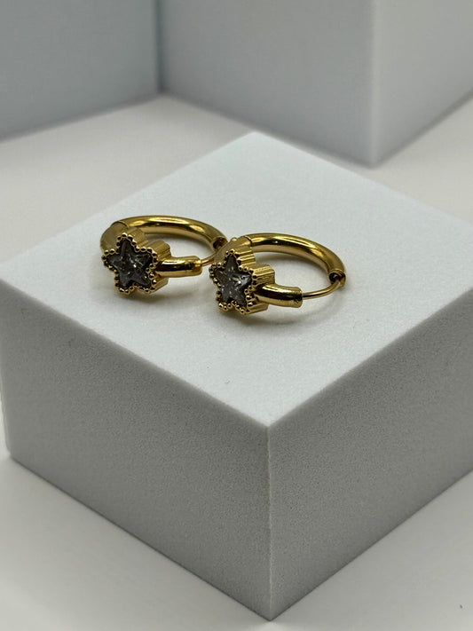 The Azure Hoops pair of gold hoop earrings with silvery gray-blue star stones displayed on white stand.