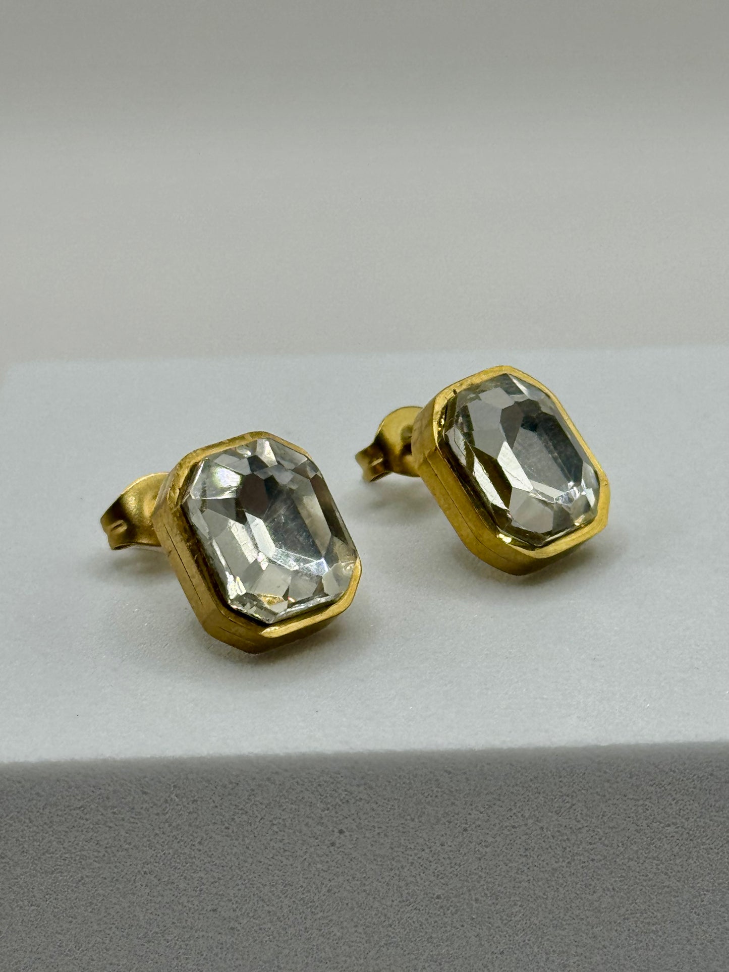A side angle of The Soleil Earrings highlighting the golden bezel and reflective glass stones.