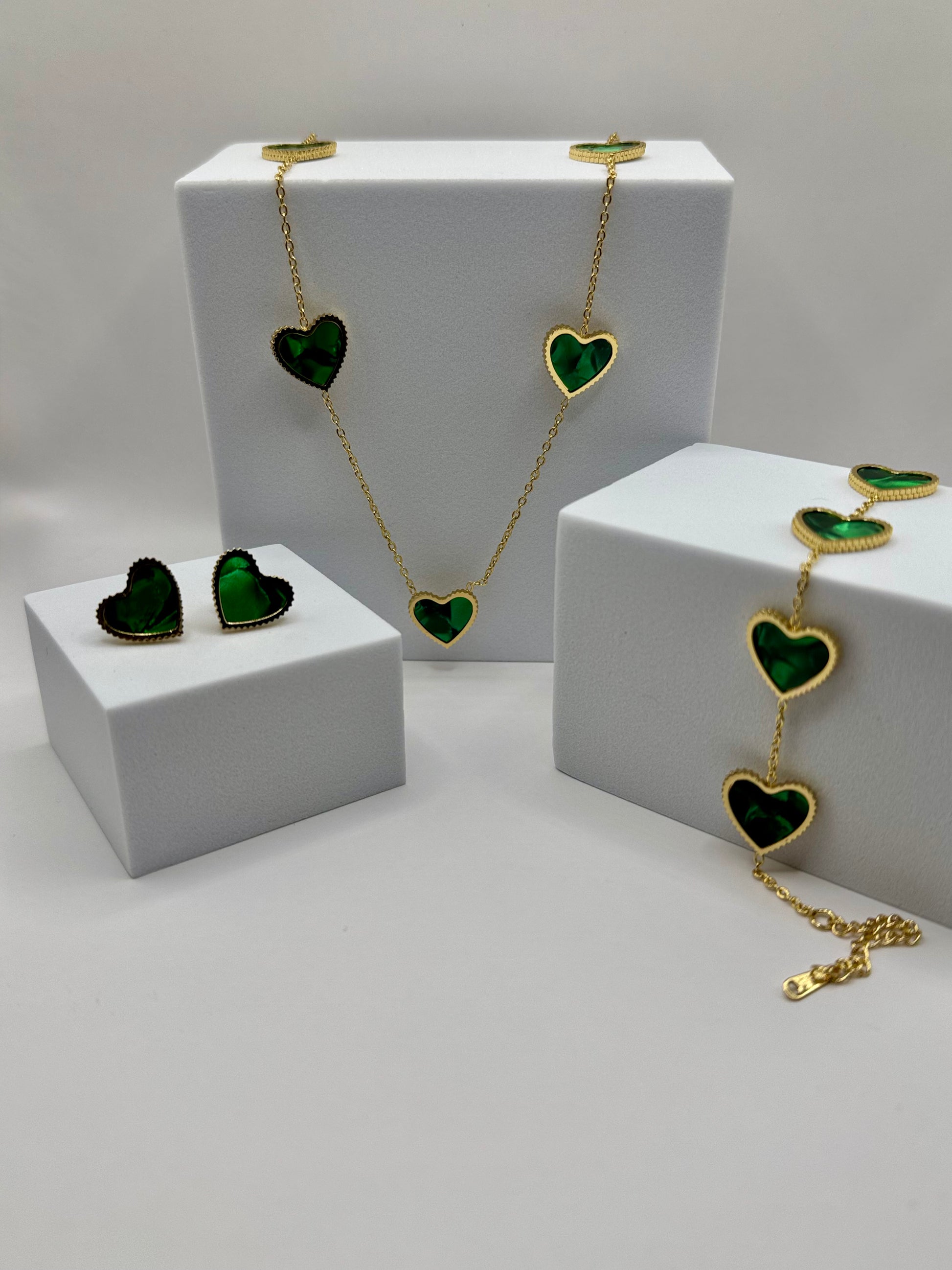 The Evergreen HEart Set complete display with necklace, bracelet, and stud earrings featuring green heart charms on white blocks.