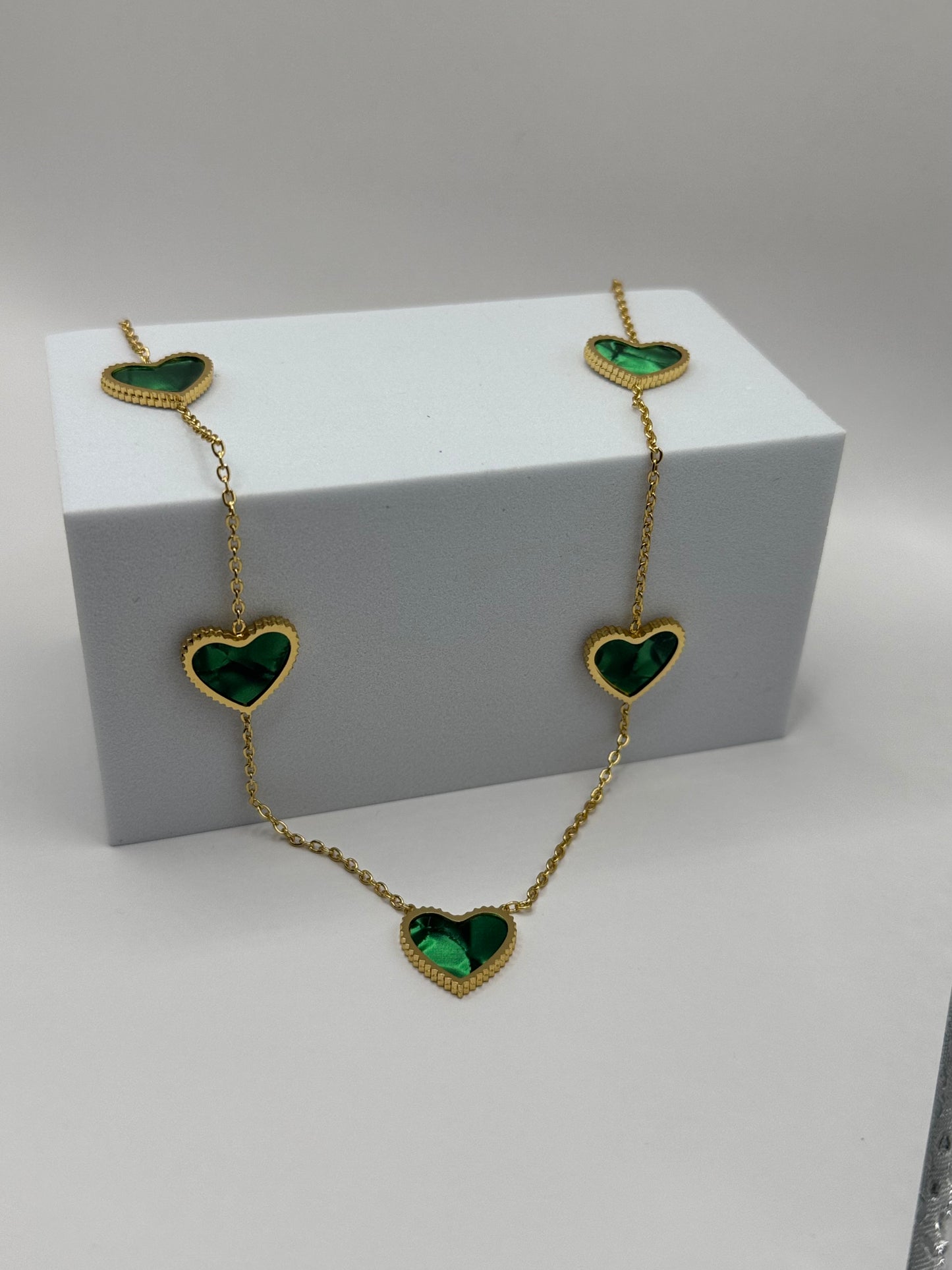 Evergreen Hearts necklace and earrings displayed on white stand with emerald green heart charms and gold-tone finish.