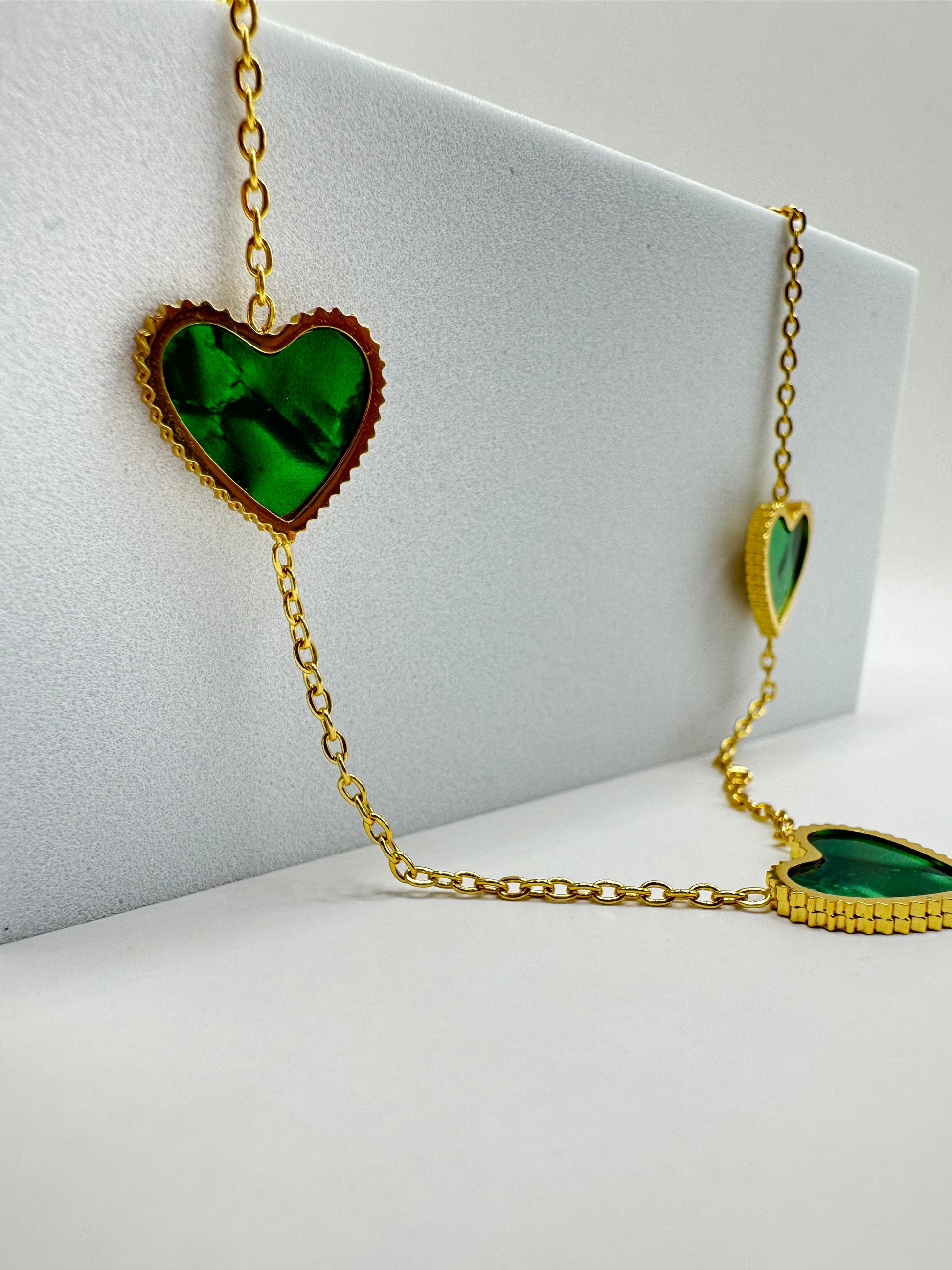 Close-up of Evergreen Hearts necklace and earrings displayed on white stand with emerald green heart charms and gold-tone finish.