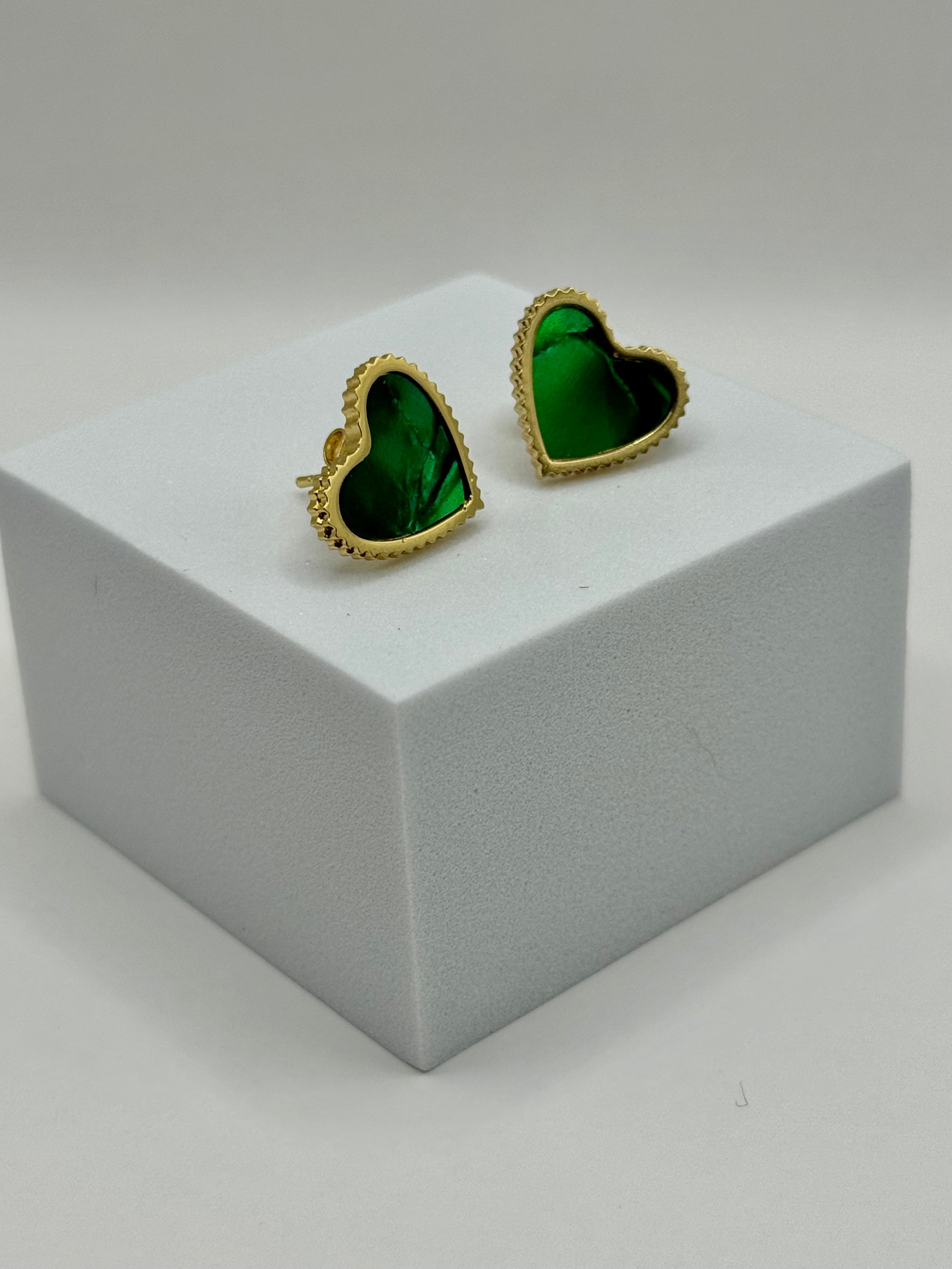 Evergreen Hearts stud earrings displayed on white block featuring emerald green hearts outlined in gold.
