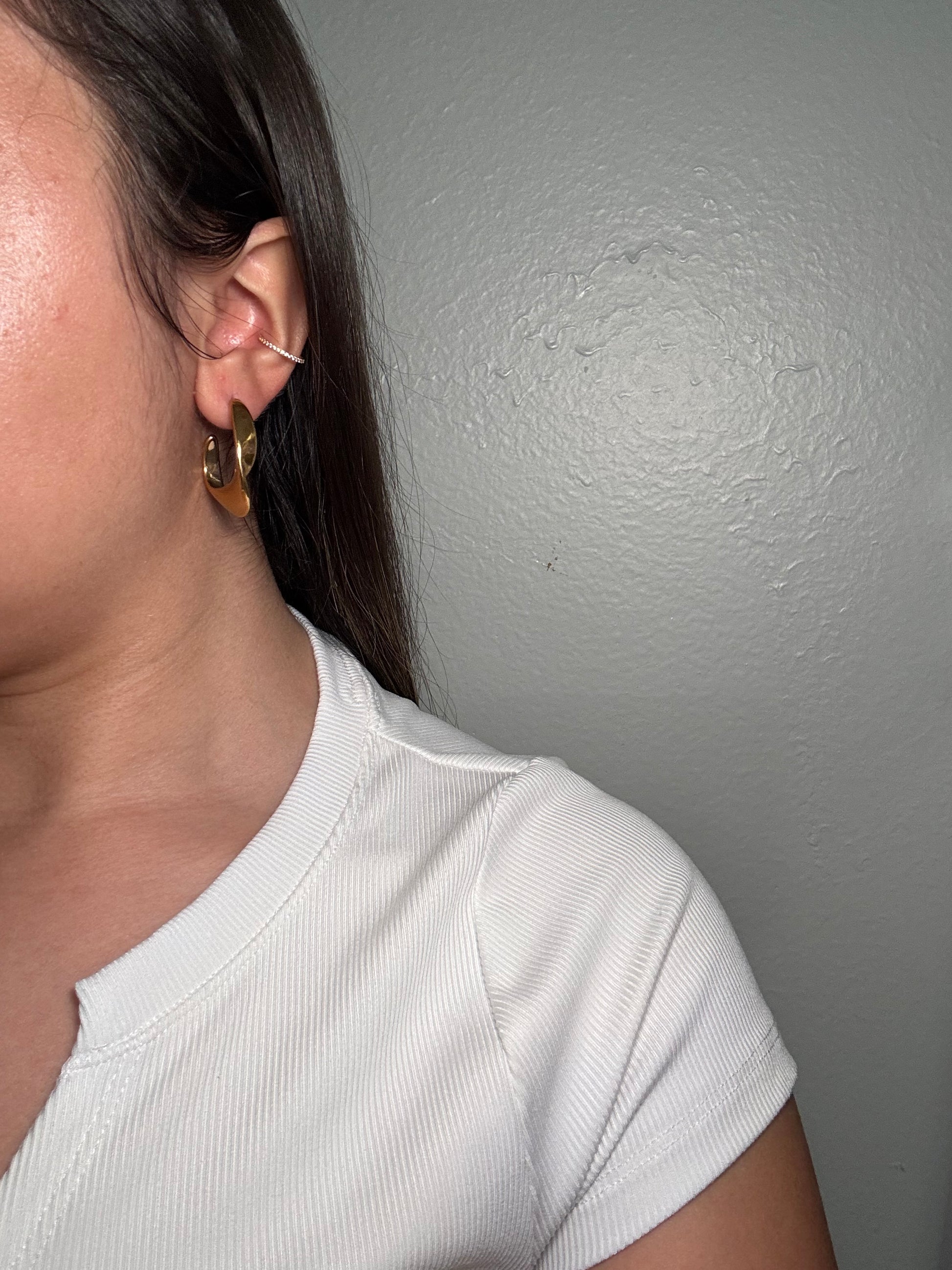 Model wearing The Virelle Earrings, showcasing gold sculptural C-shaped hoops styled with soft luxe finish.