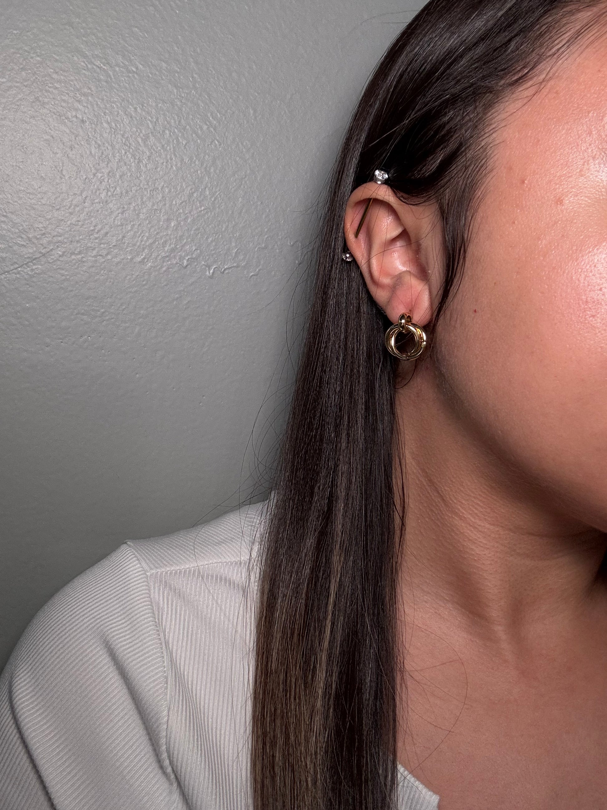 The Entwined Earrings worn by model close-up on ear showing double-ring gold studs for size and style reference.