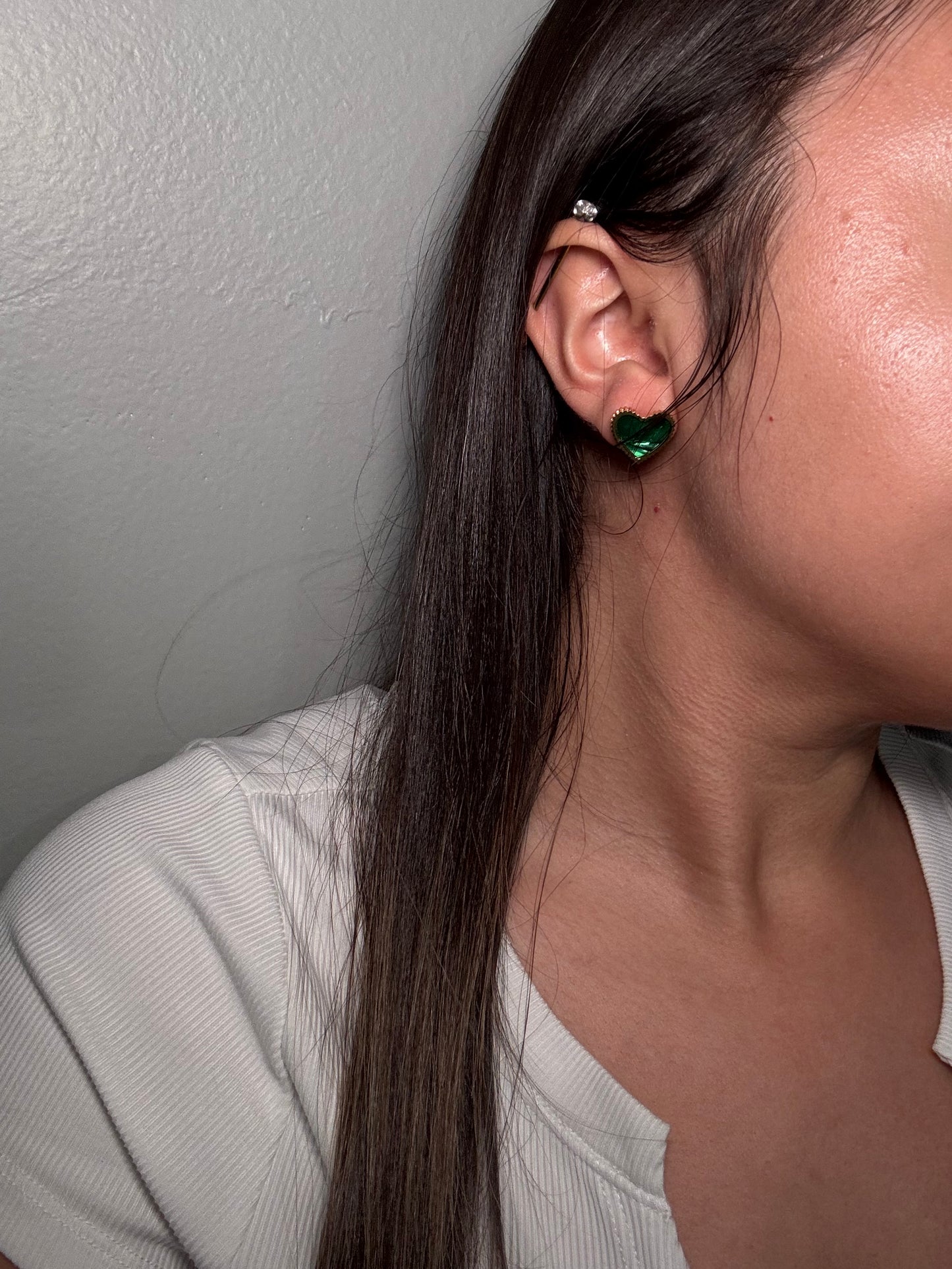 Evergreen HEarts stud earrings worn by model close-up on ear showing emerald green hearts outlined in gold.