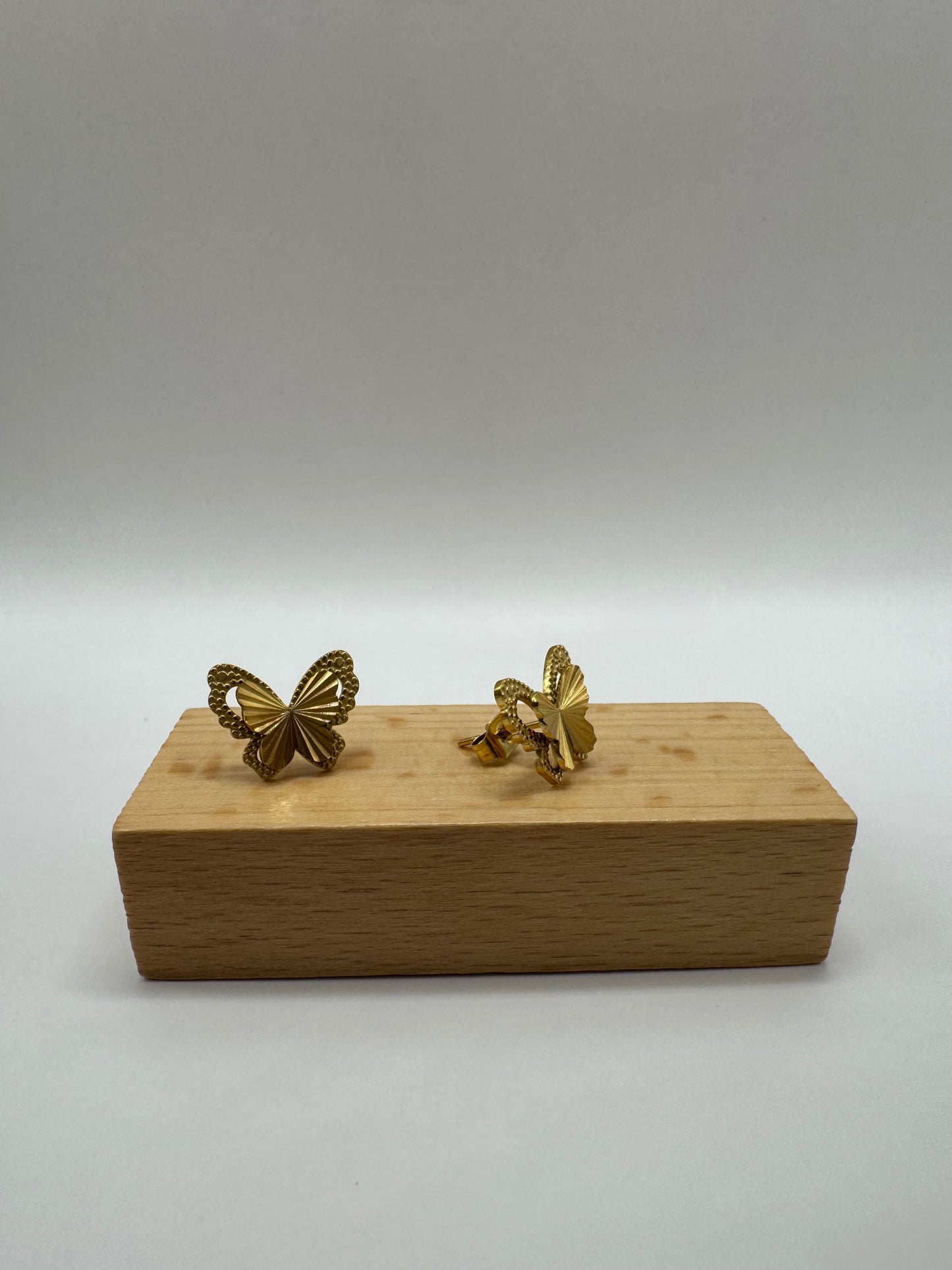Gold butterfly stud earrings and necklace presented on a small brown wooden bock.