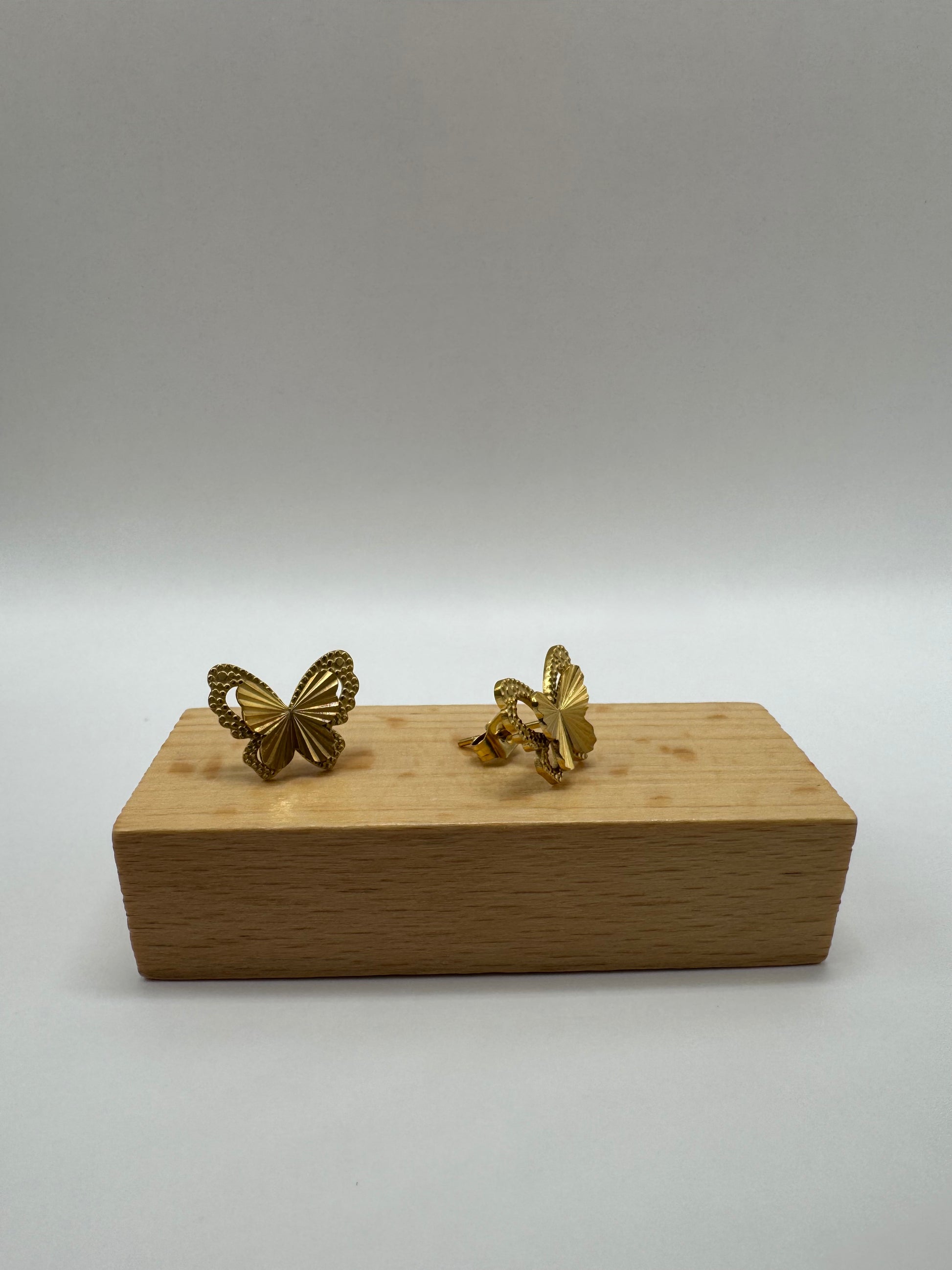 Gold butterfly stud earrings and necklace presented on a small brown wooden bock.