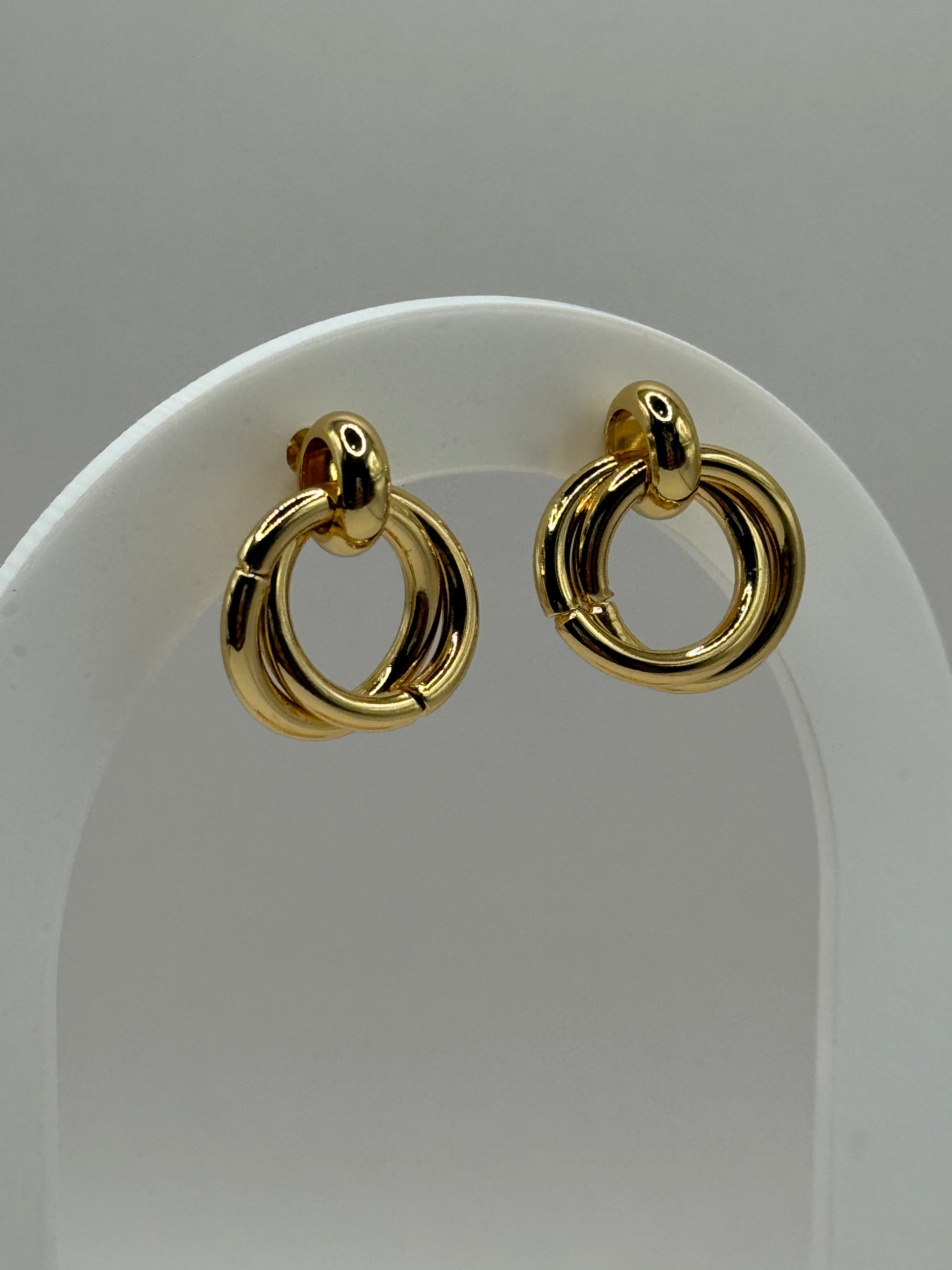 The Entwined Earrings displayed upright on white stand showing sculptural double-ring design and polished gold finish.