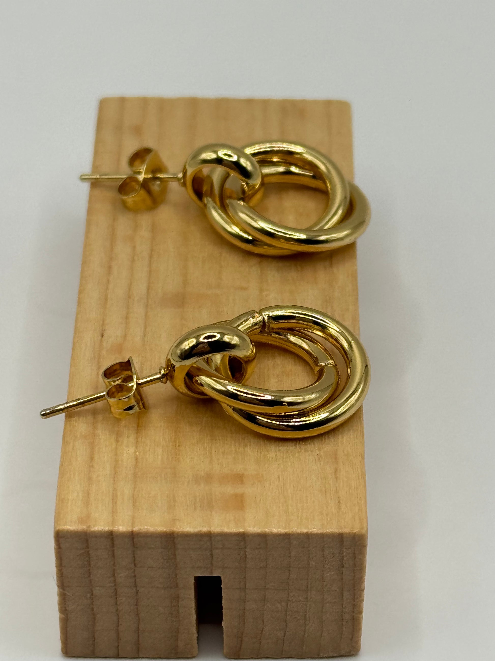The Entwined Earrings displayed flat on wooden block close-up of gold-ring design with stud backing visible.