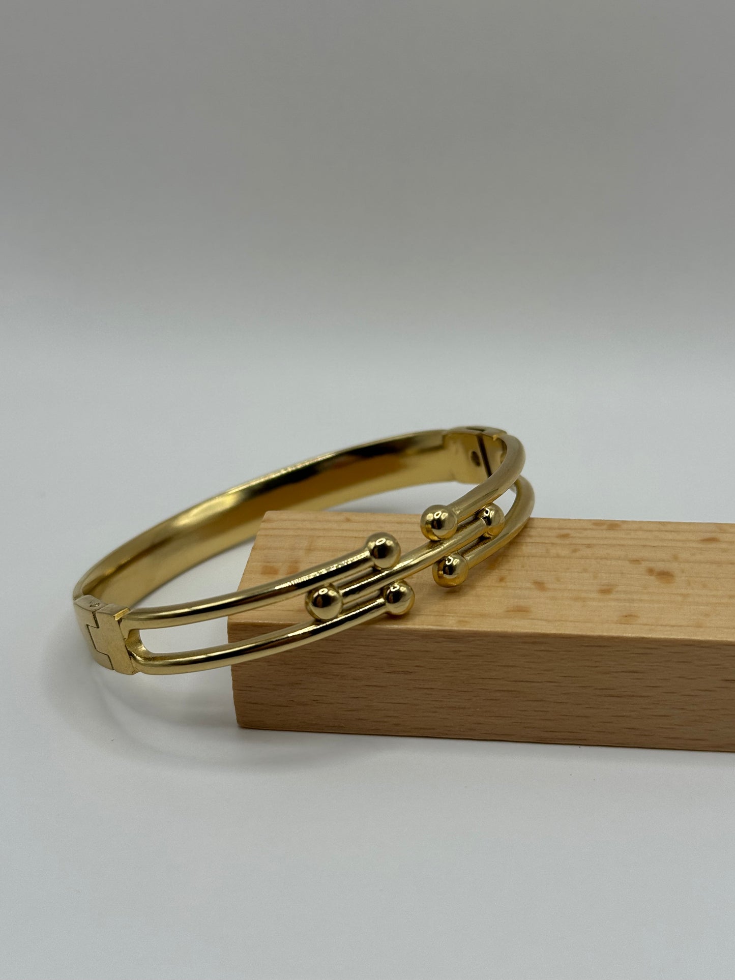Side view of The Colette Bracelet resting on a wooden stand, highlighting the slim bangle design.