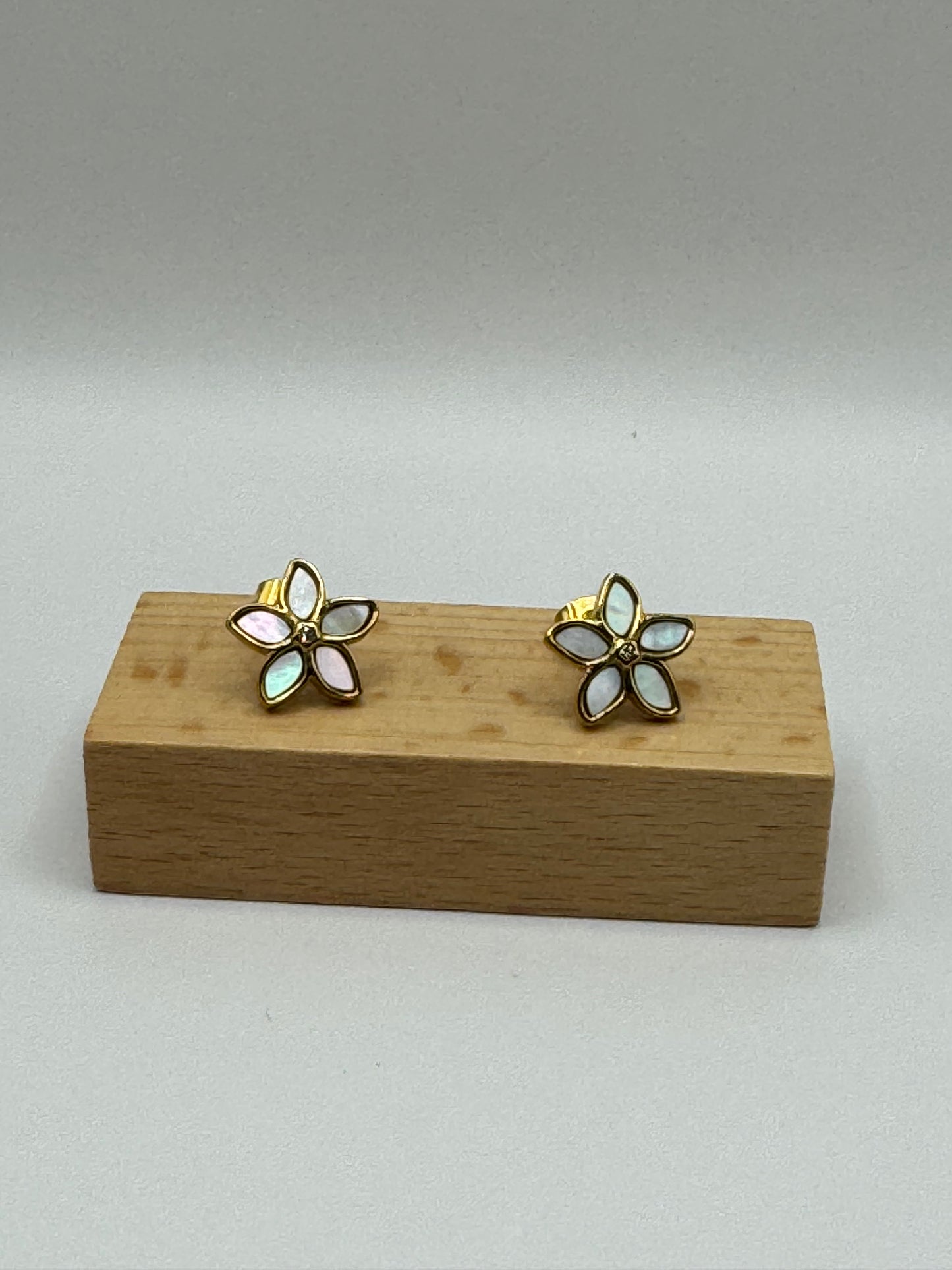 The Opalina floral stud earrings displayed on wooden earring block highlighting enamel petals outlined in gold.