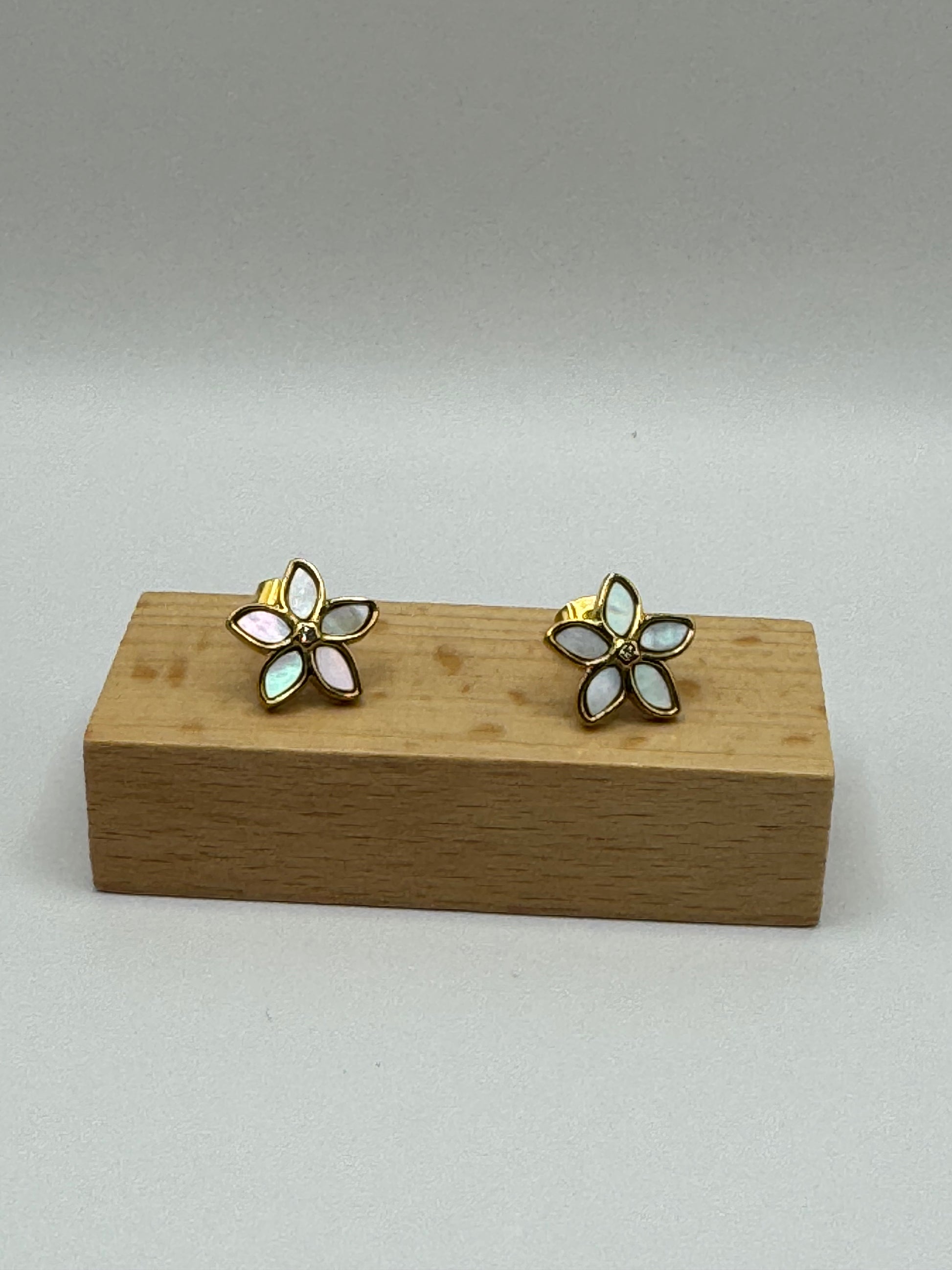 The Opalina floral stud earrings displayed on wooden earring block highlighting enamel petals outlined in gold.