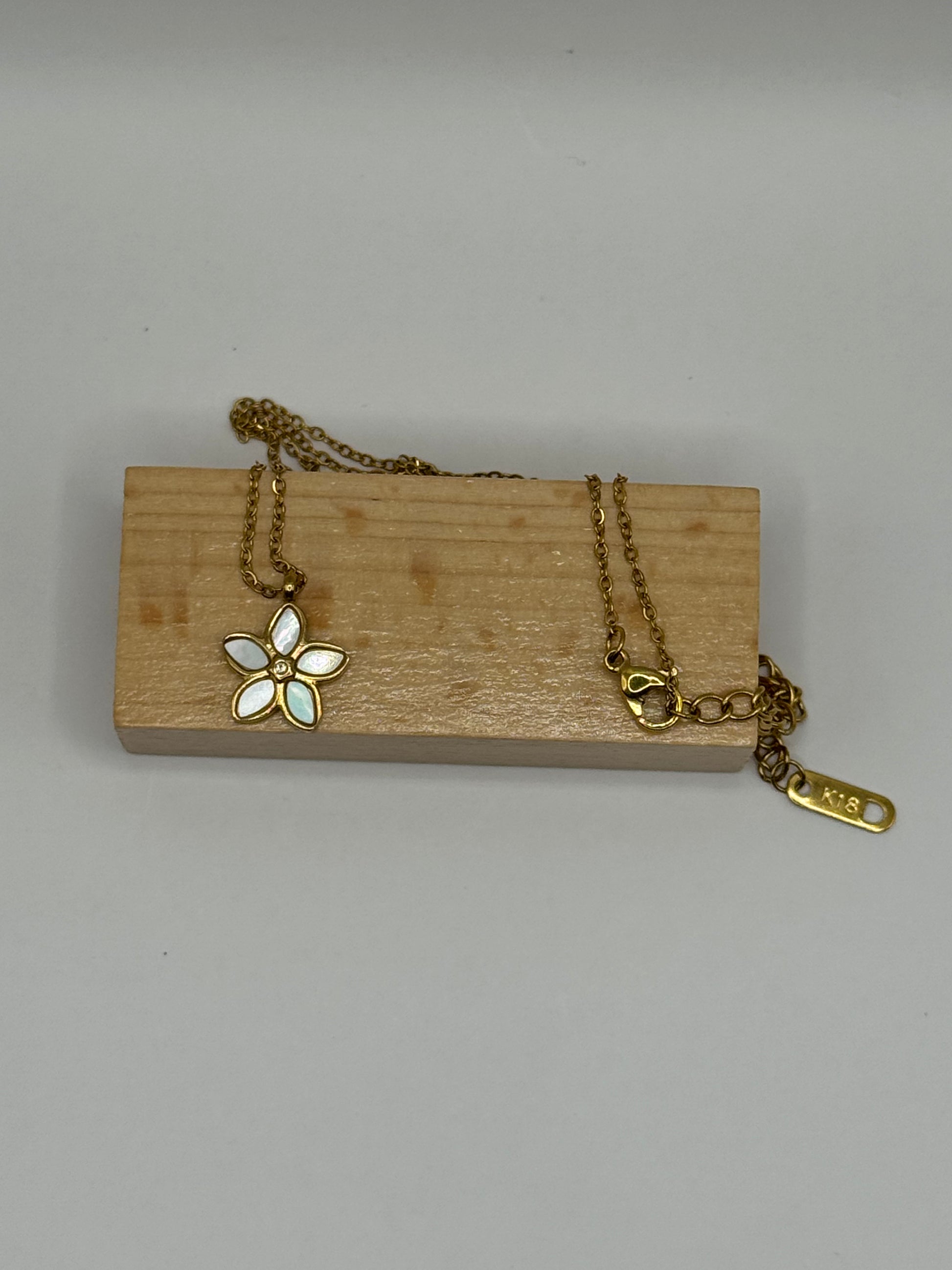 The Opalina necklace with floral pendant displayed on branded brown jewlery box with gold chain draped across.