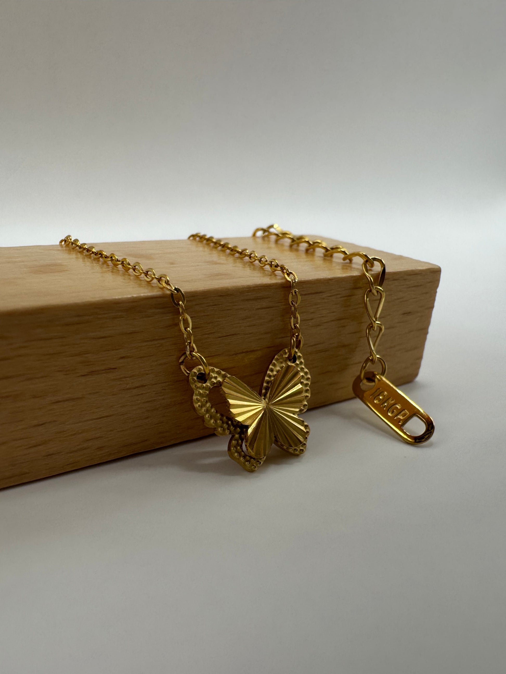 Close-up Aurora Clásica gold butterfly necklace displayed on wooden block with chain and clasp visible.