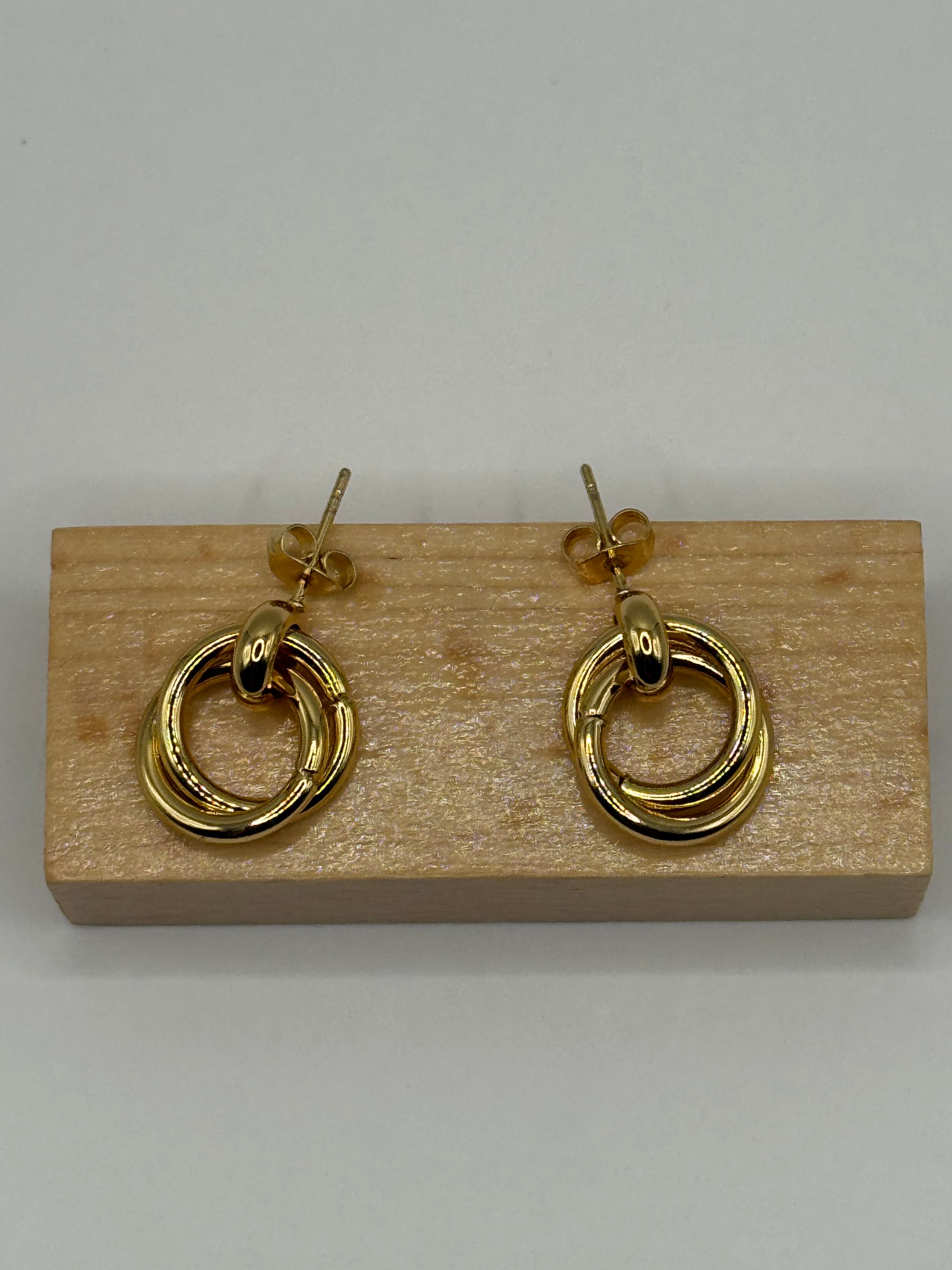 The Entwined Earrings haning on wooden earring block highlighting circular double-ring structure and shine.