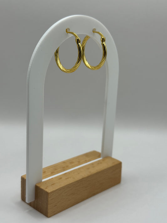 The Cinta Twist earrings displayed on a white jewelry stand with wooden base, highlighting their twisted design and radiant gold plating.