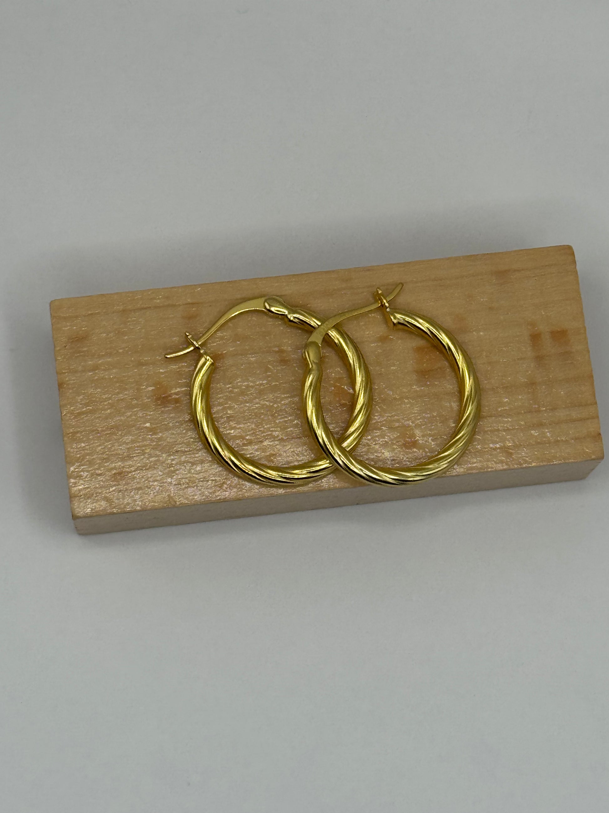 Close-up of The Cinta Twist earrings resting on a wooden block, showcasing their interwoven gold-tone detailing.