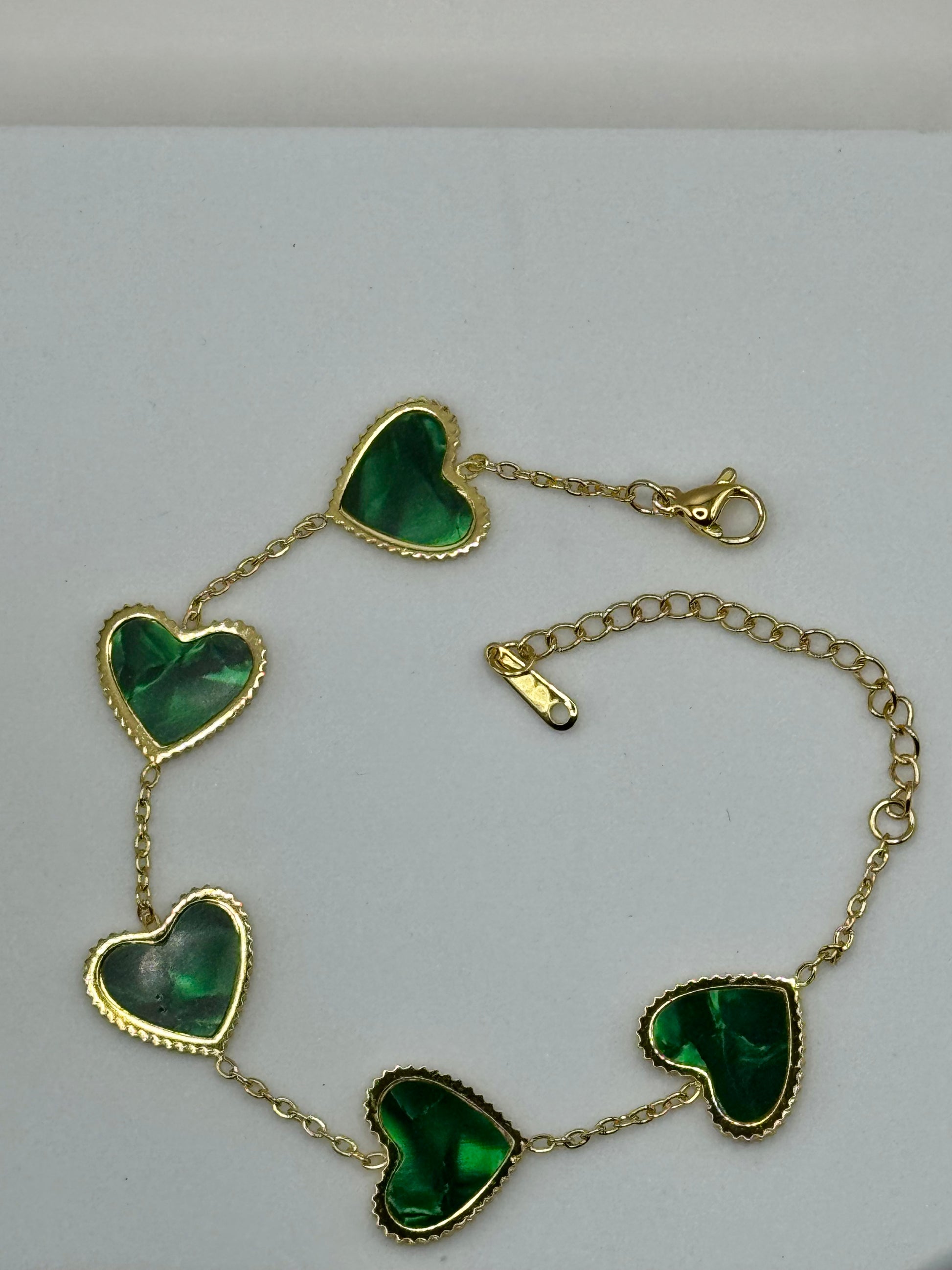 Evergreen Hearts bracelet close-up of green heart charms and gold-tone chain on white block.