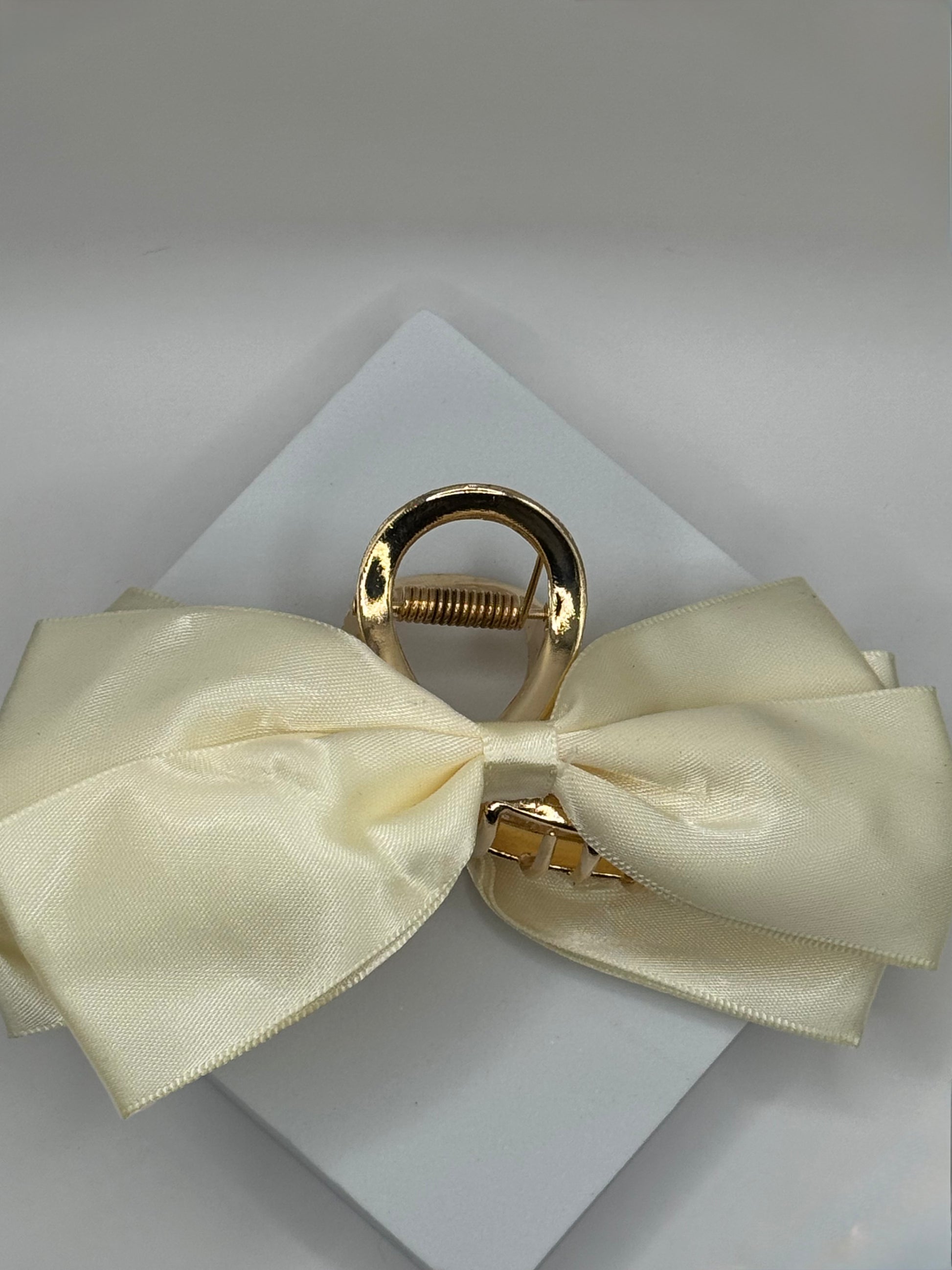 Side angle of EMPIECE™ Paloma Hair Clip in ivory satin bow with gold claw closure.