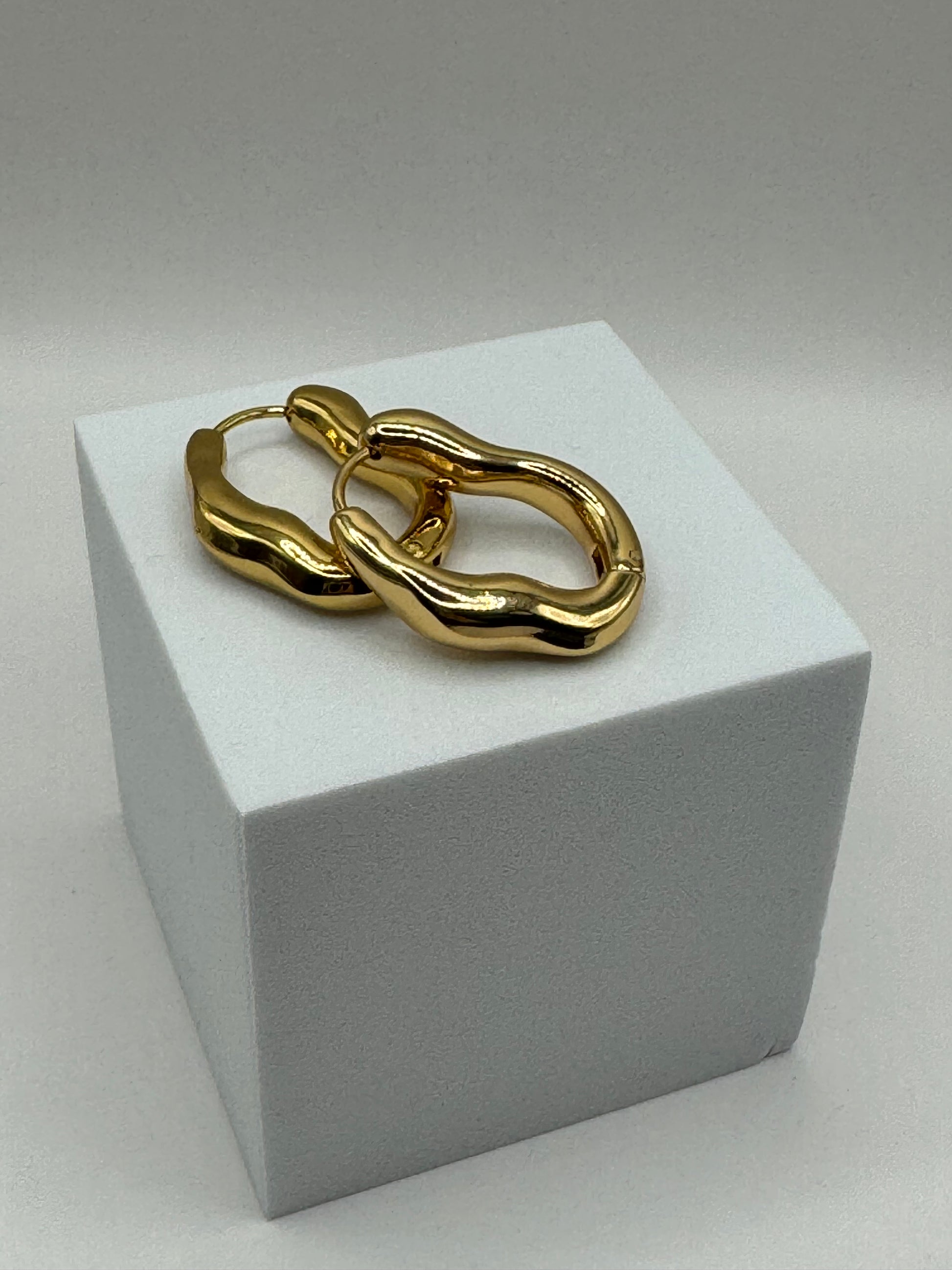 Side view of The Alinéa Hoops gold sculptural earrings on white block.