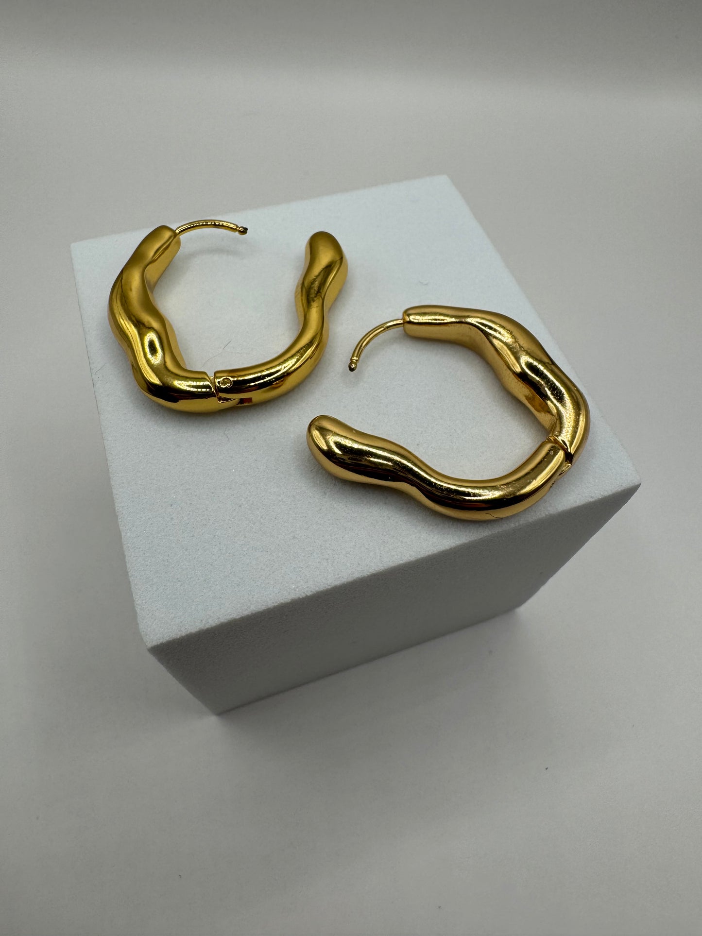 Angled view of The Alinéa Hoops gold-toned earrings highlighting polished wavy form.