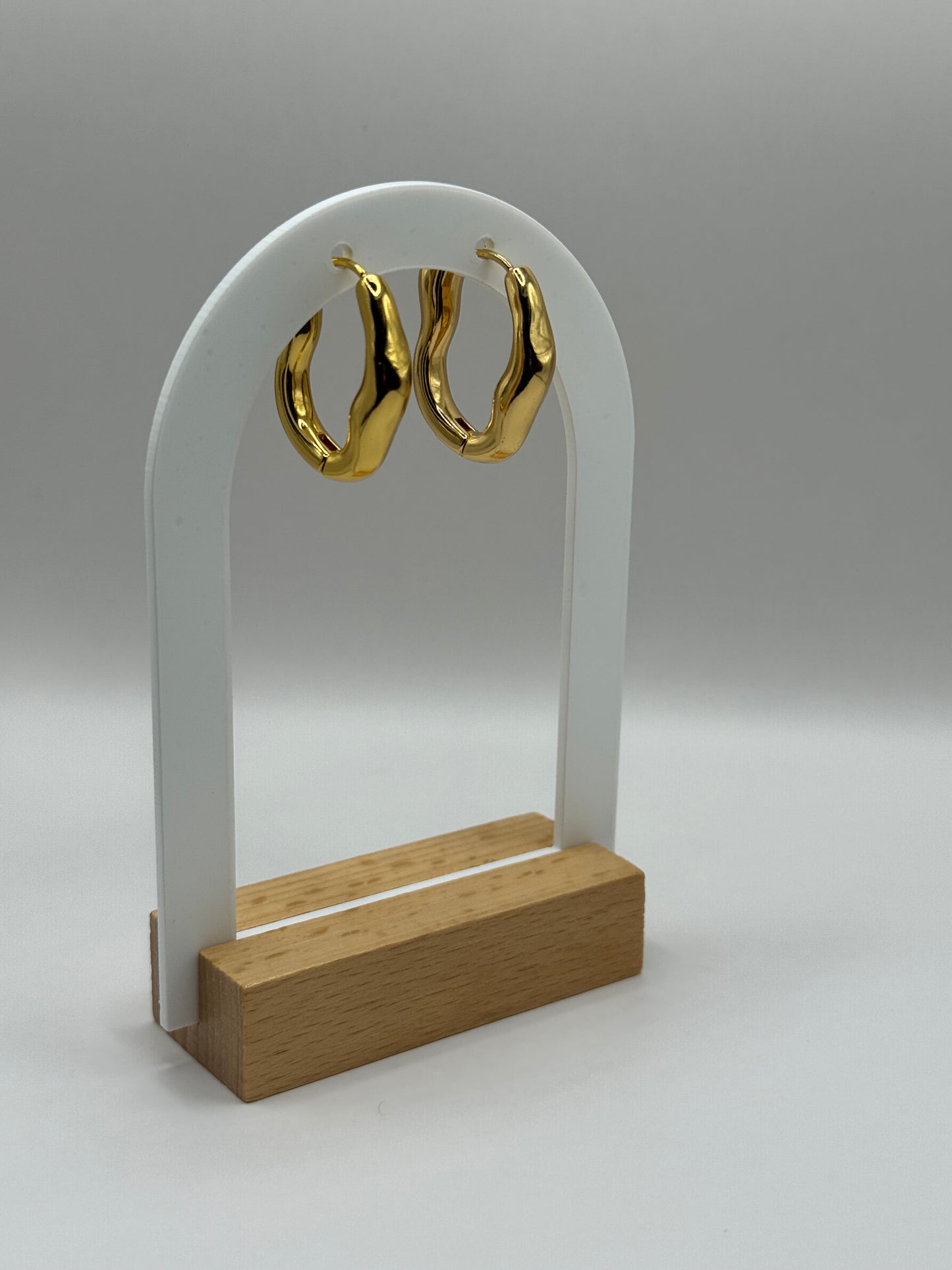 EMPIECE™ The Alinéa Hoops displayed on jewelry stand with gold base showing modern wavy shape.