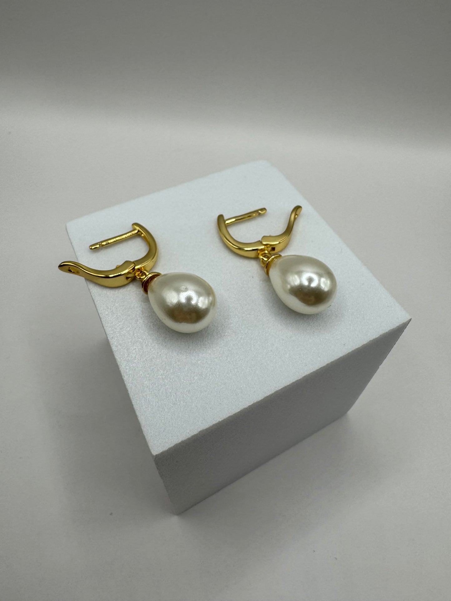 Angled view of The Amara Earrings on white block highlighting gold-plated hoop and pearl design.
