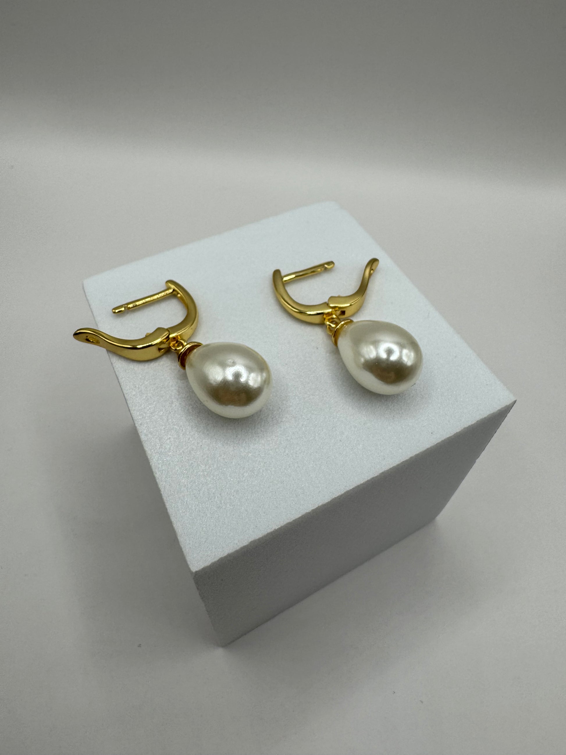 Angled view of The Amara Earrings on white block highlighting gold-plated hoop and pearl design.