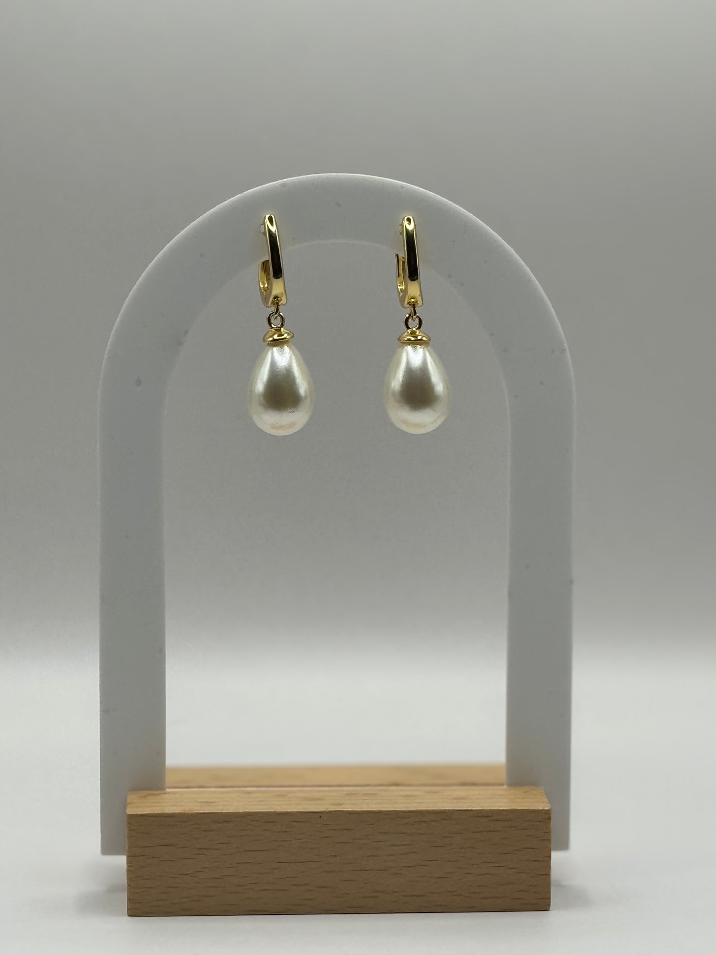 The Amara Earrings displayed on jewelry stand with gold hoops and pearl accents.