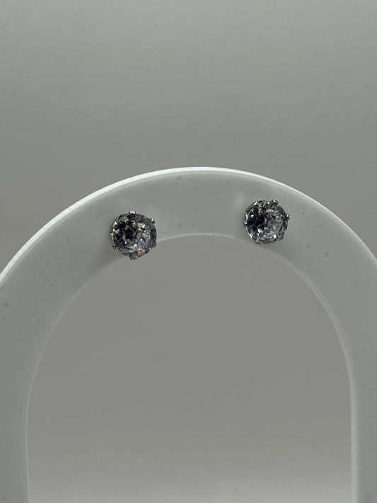 Silver cubic zirconia stud earrings displayed on a clear curved stand, The Ari Studs by EMPIECE™.