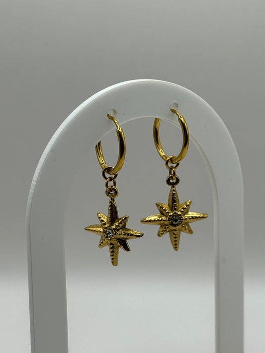 The Meridian Star gold huggie earrings with star charm and CZ center displayed on a curved stand.
