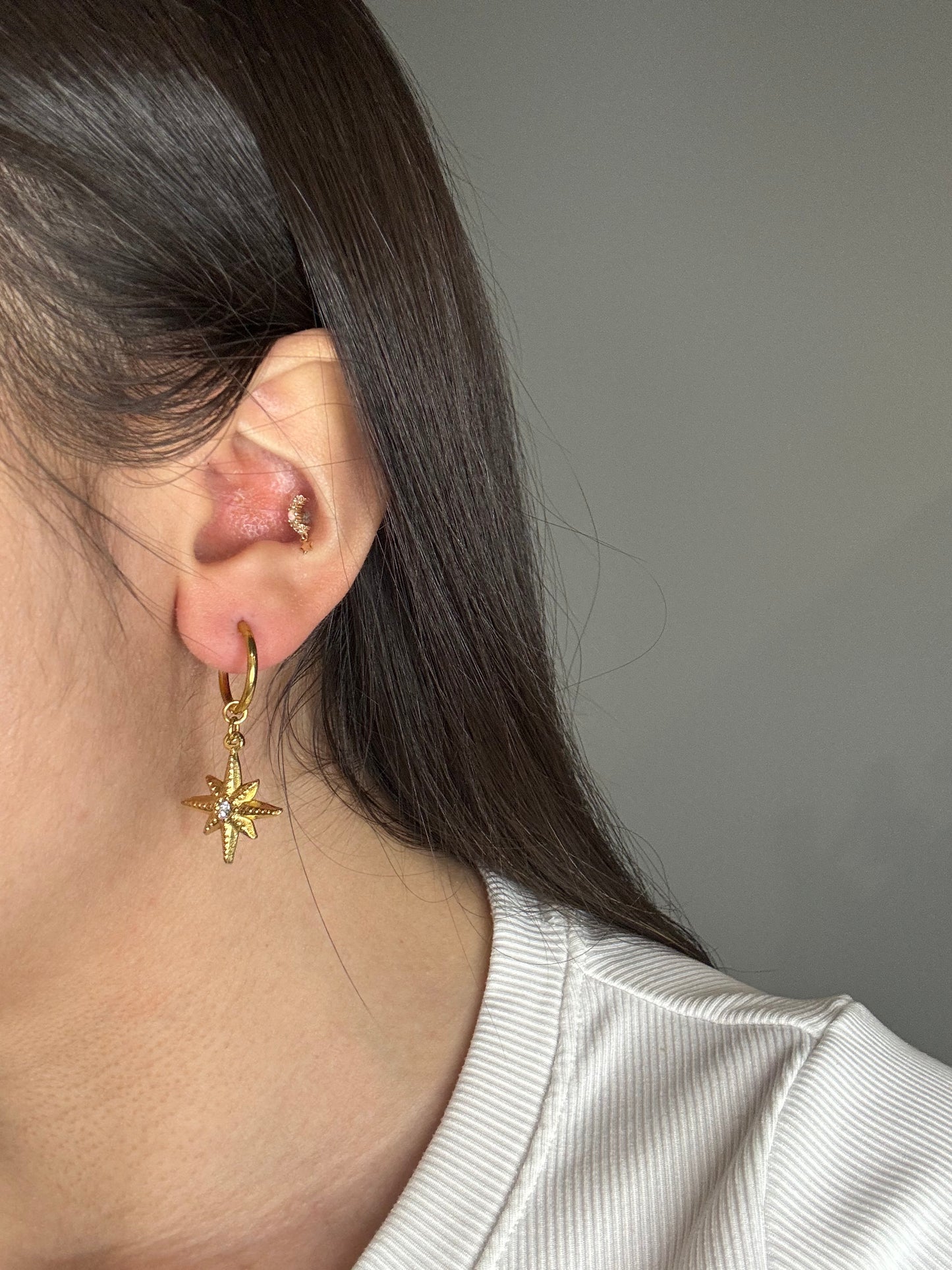 The Meridian Star gold huggie earrings worn on ear, featuring a star charm with CZ center.