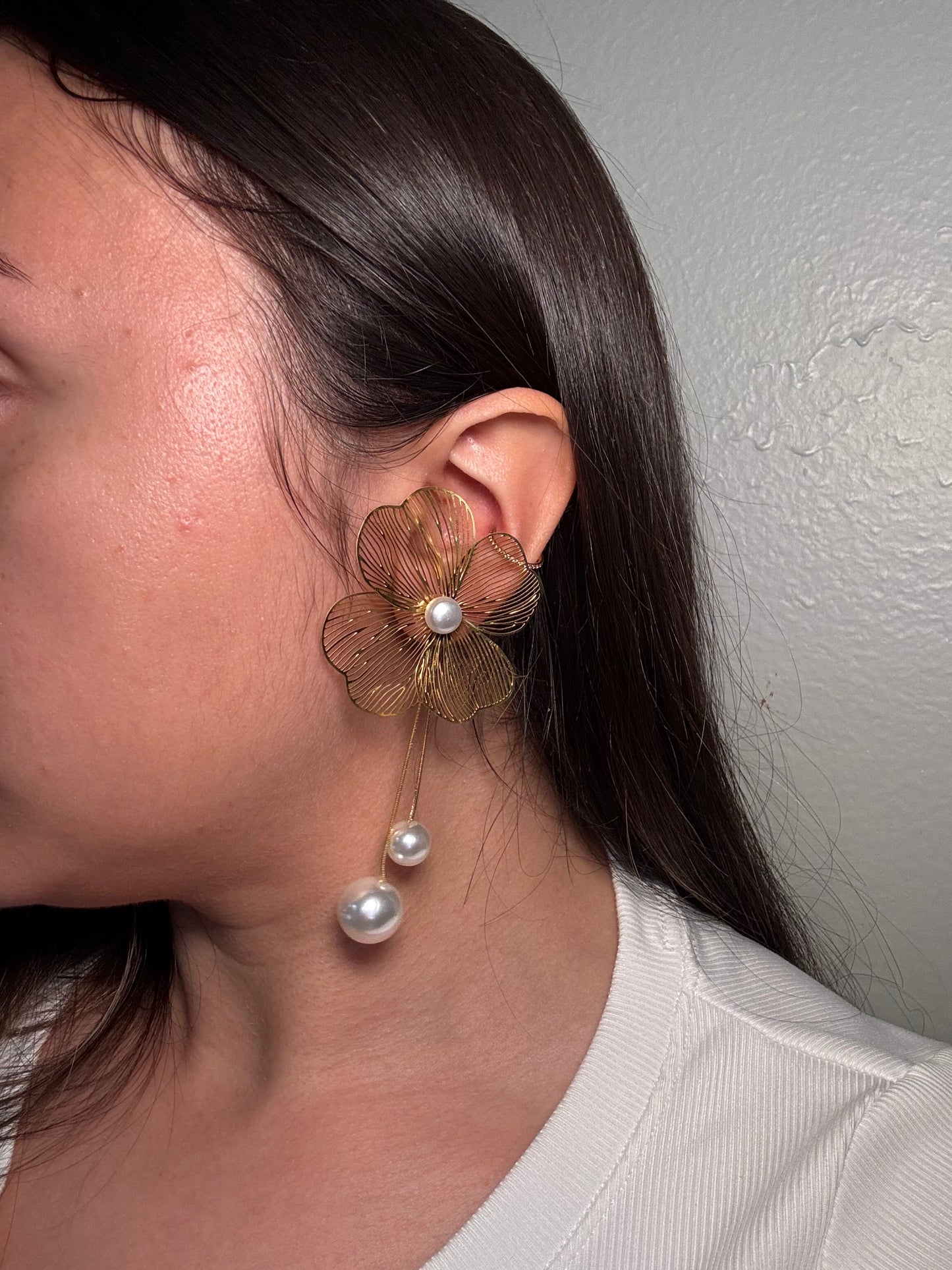 Model wearing The Nerina Earrings, showcasing gold floral petals with pearl center and drop.