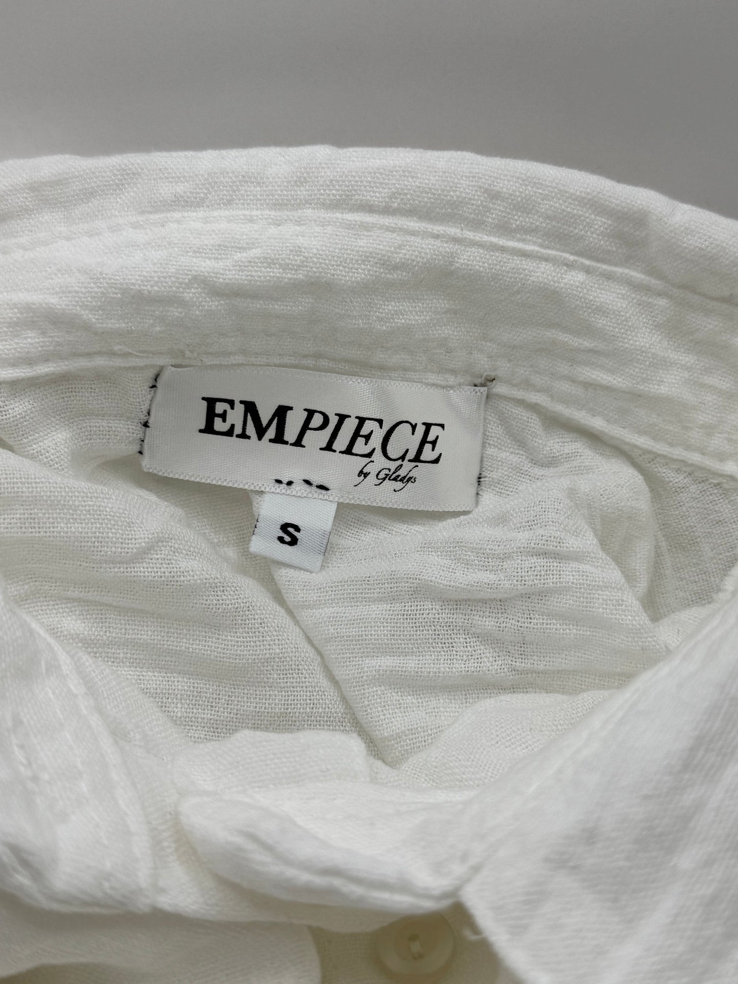 Close-up of EMPIECE™ by Gladys woven label sewn inside The Clarity Whisper Top in white fabric.