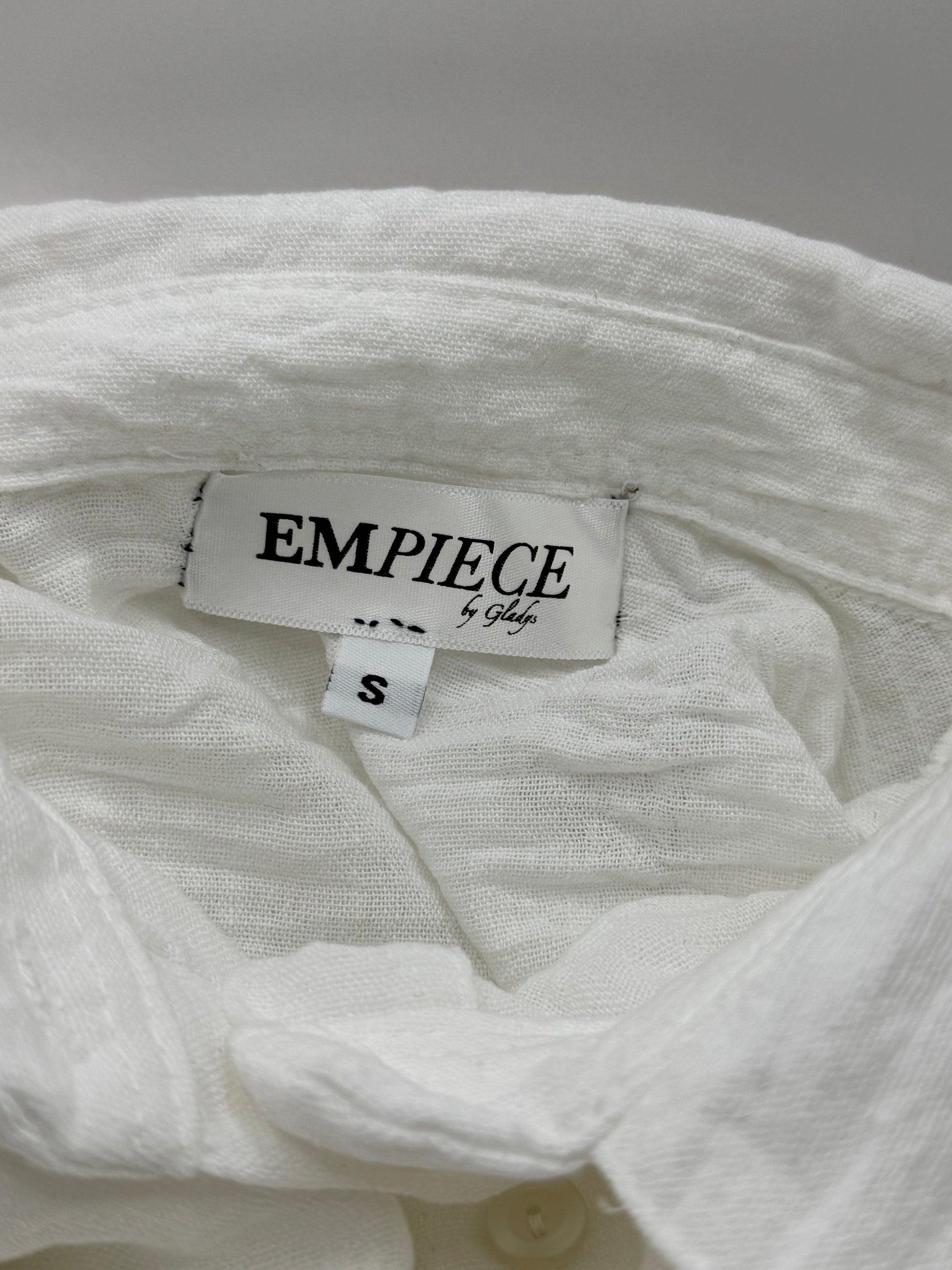 Close-up of EMPIECE™ by Gladys woven label sewn inside The Clarity Whisper Top in white fabric.