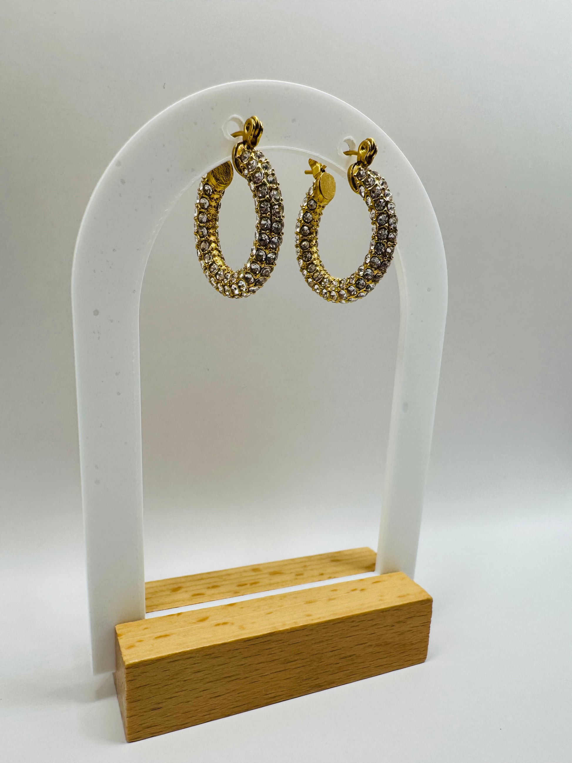 Aros Novina hoop earrings displayed on white jewelry stand with gold base.