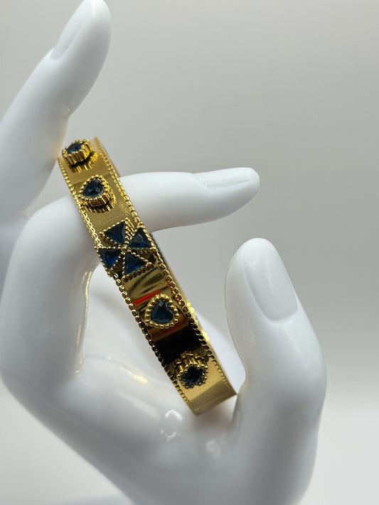 Close-up of The Noctara Bracelet held in hand, showcasing gold bangle with cobalt star and teardrop motifs.