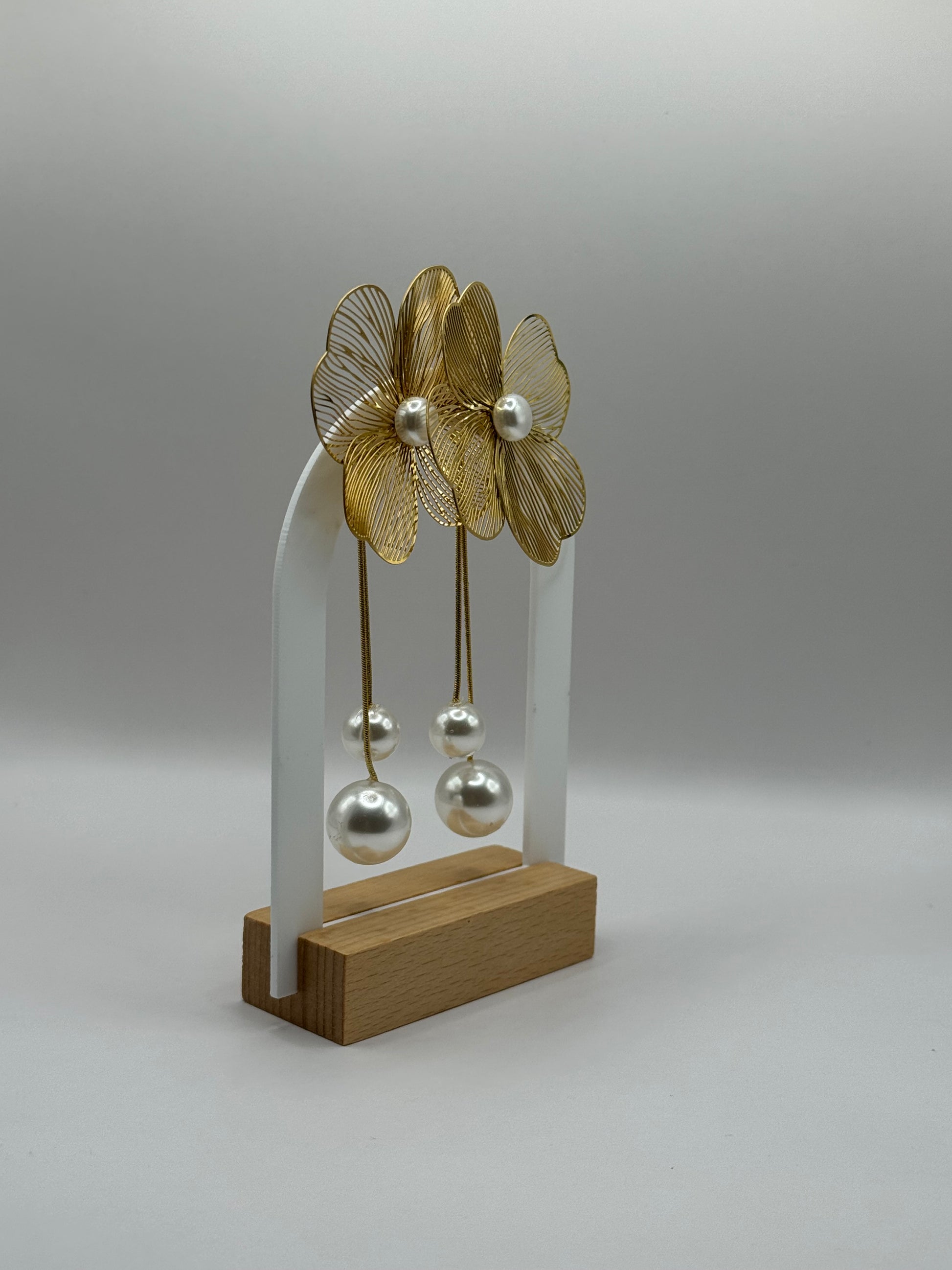 The Nerina Earrings displayed on jewelry stand showing gold-plated flower design with pearl accents.
