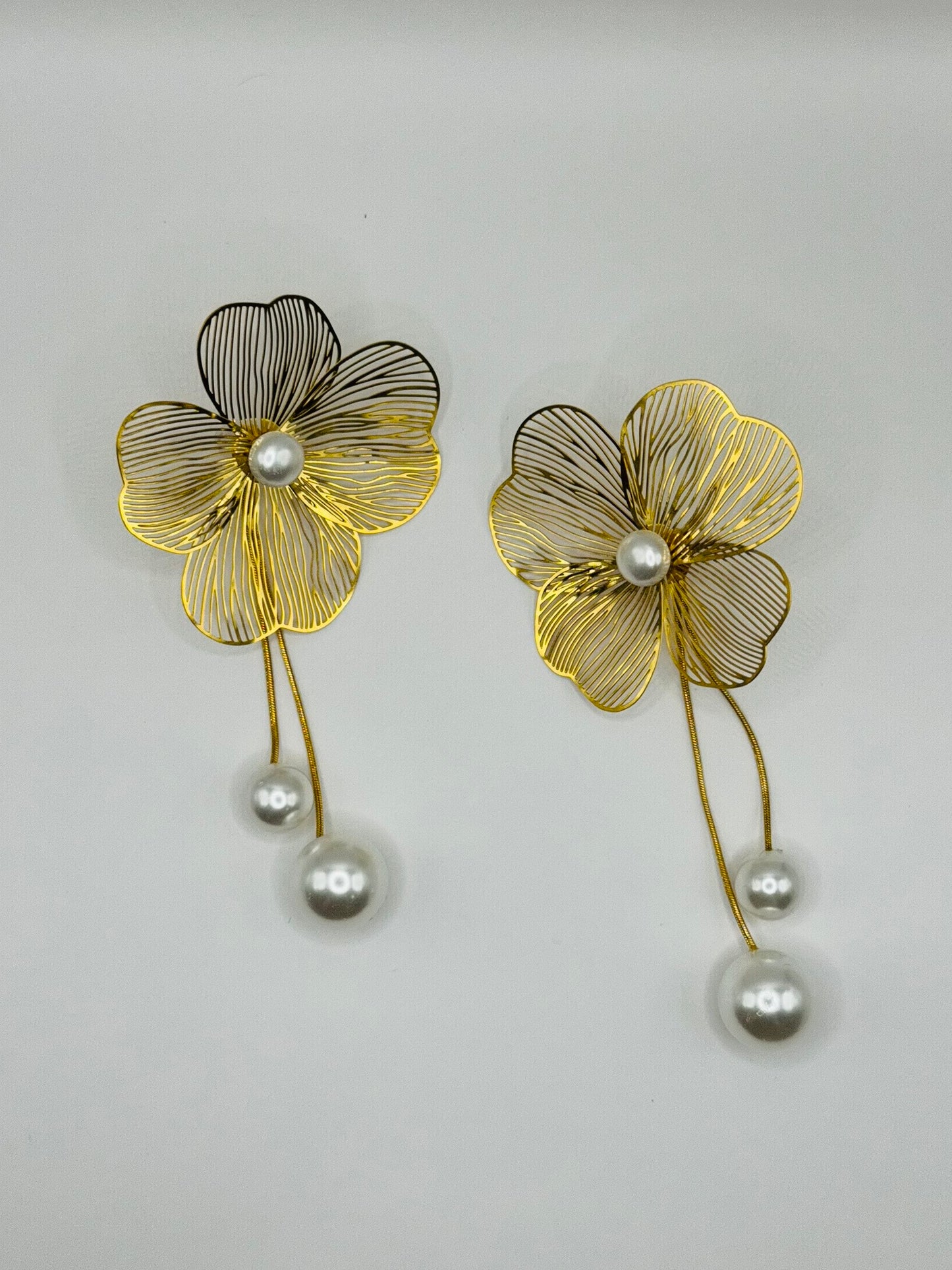 Close-up of The Nerina Earrings featuring gold floral petals with pearlcenter and drop detail on white background.