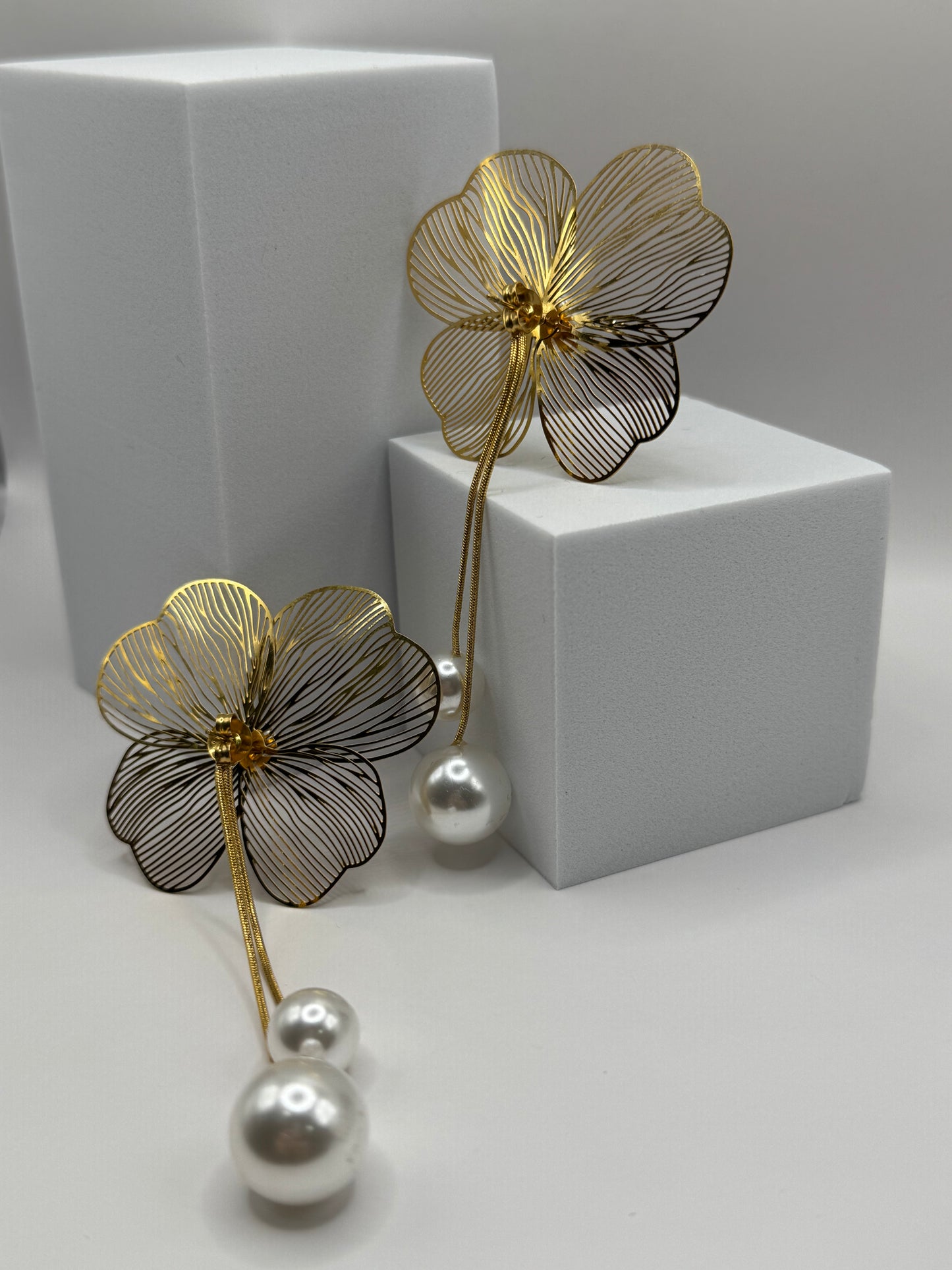 Angled view of The Nerina Earrings on white block highlighting sculptural petal and pearl drop design.