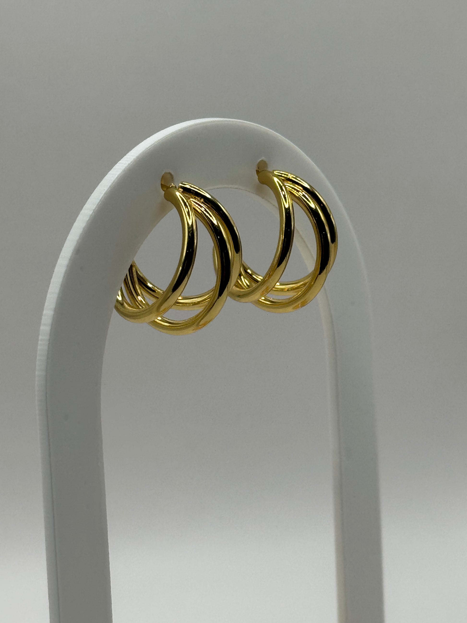 Gold stacked huggie hoop earrings displayed on a minimalist stand