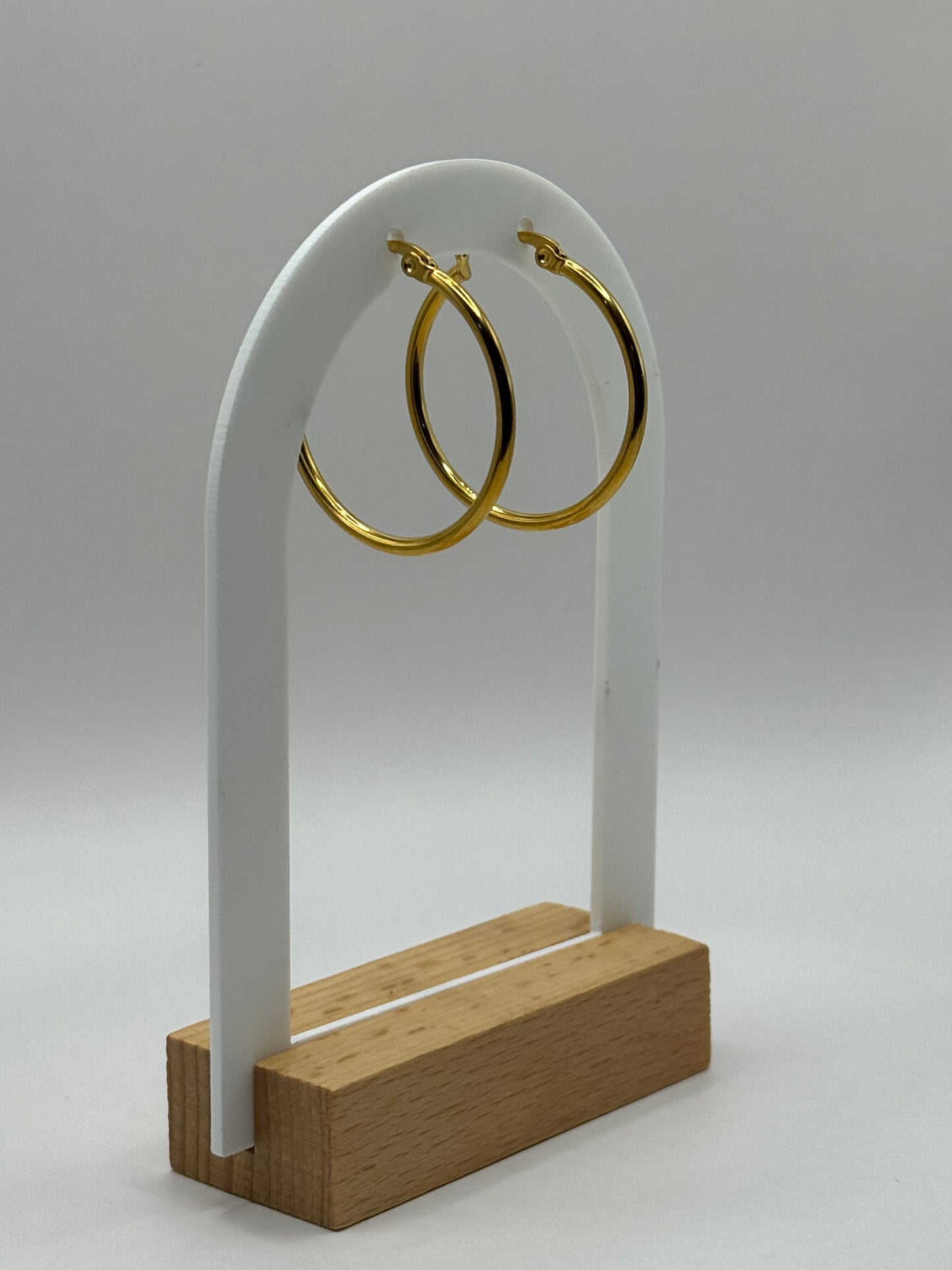 Gold hoop earrings displayed on a white acrylic stand with a wooden base