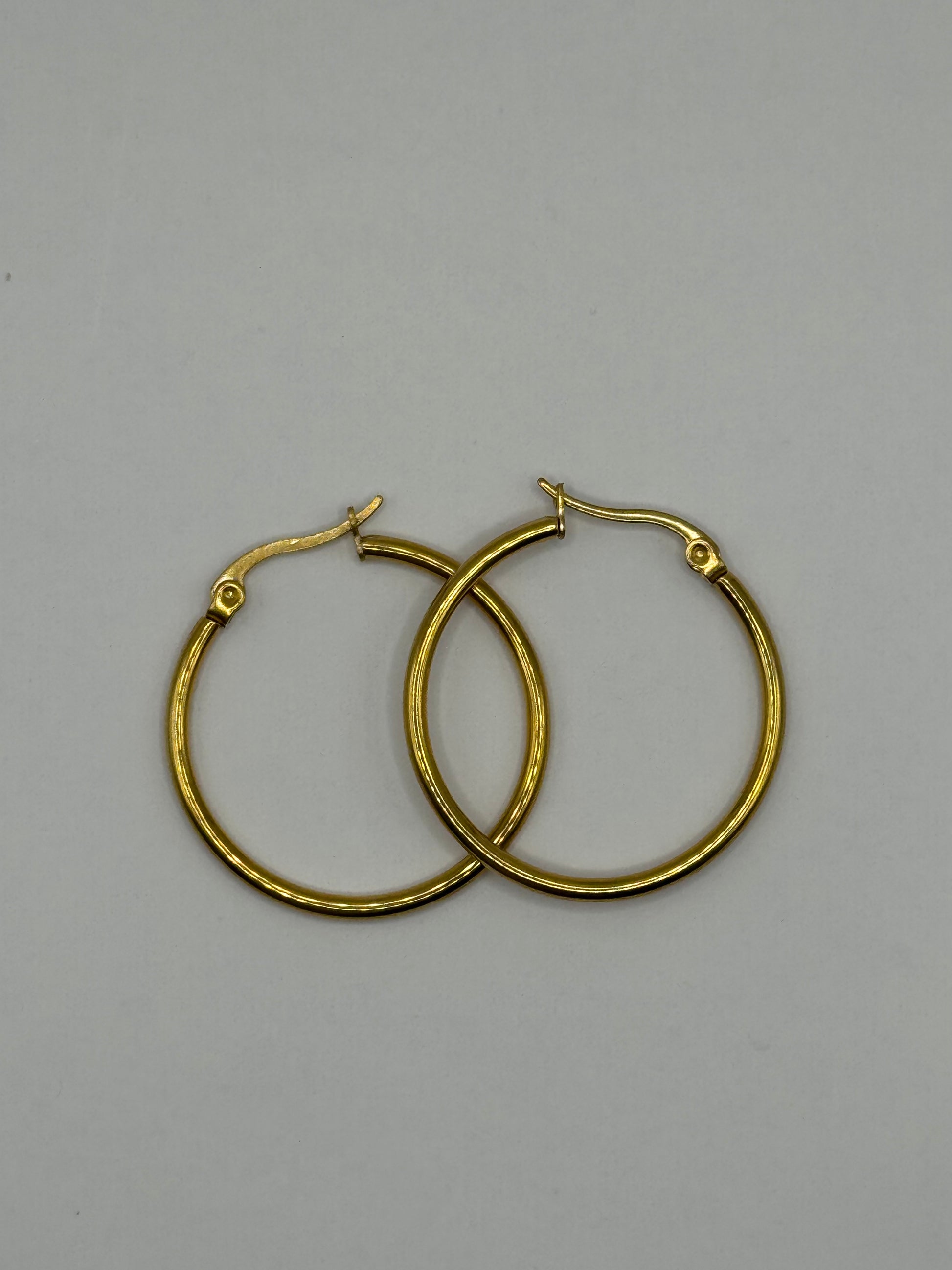 Gold hoop earrings laid flat on a light gray background