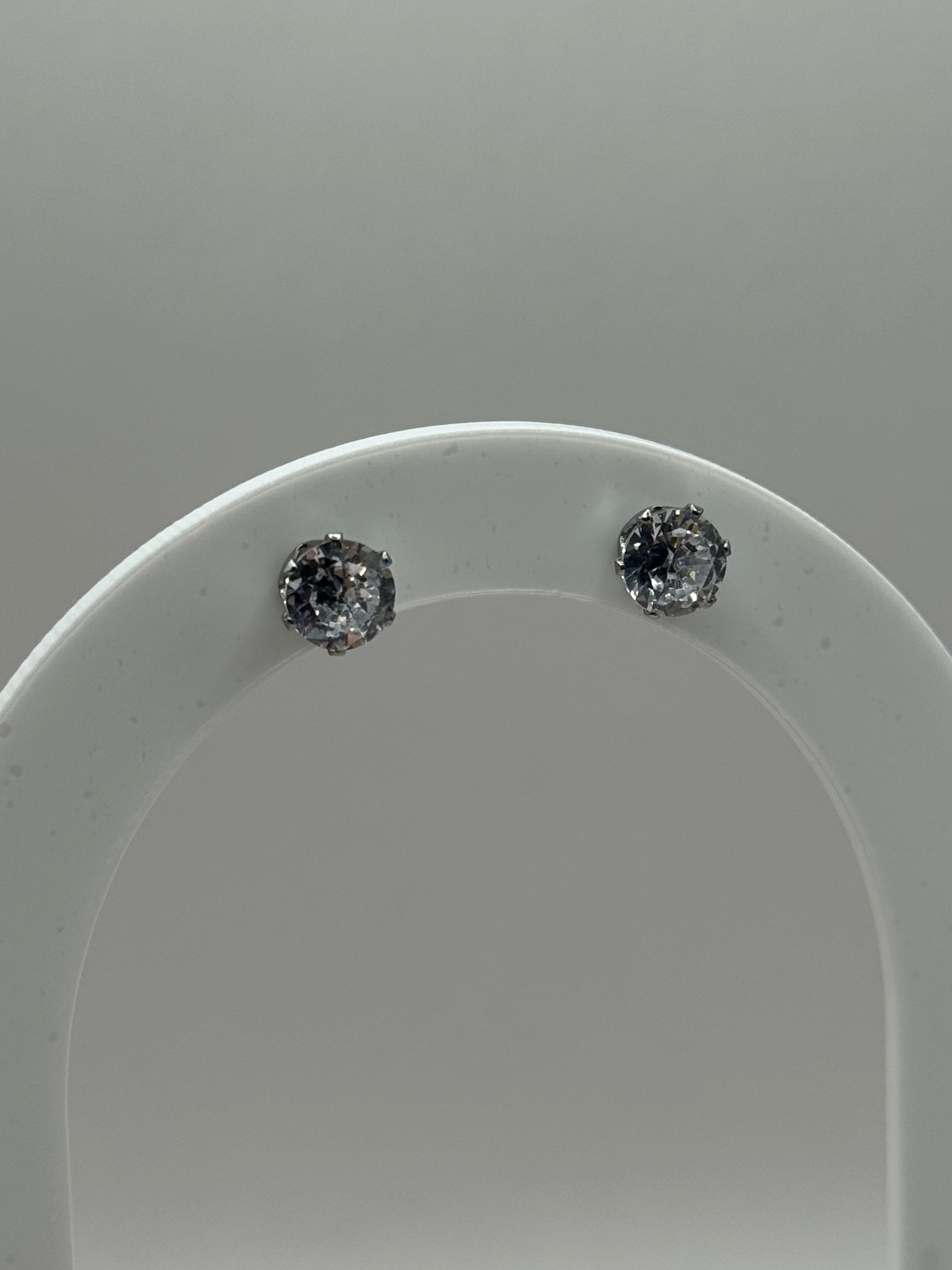 Silver cubic zirconia stud earrings displayed on a clear curved stand, The Ari Studs by EMPIECE™.