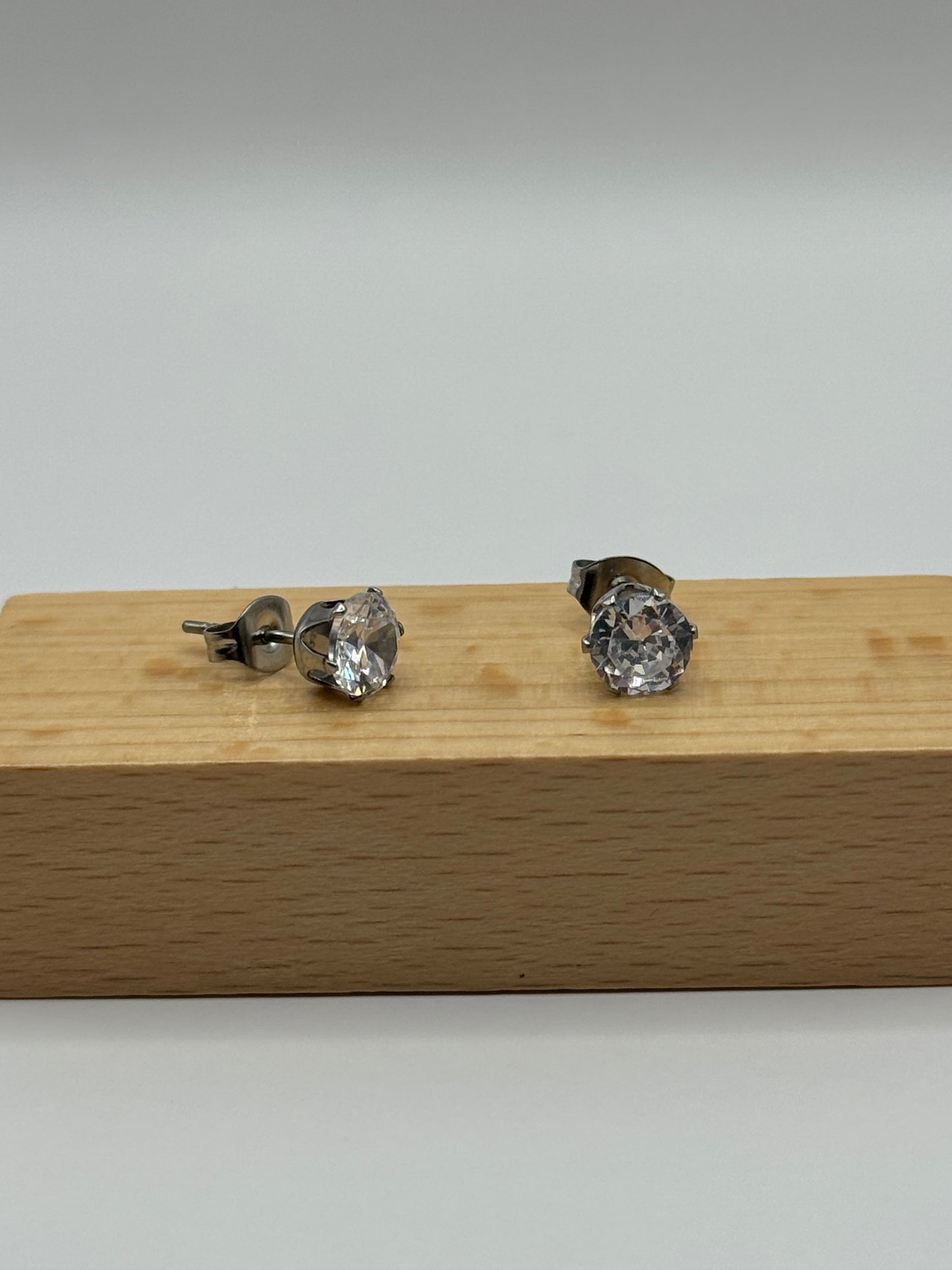 Silver cubic zirconia stud earrings shown from a side angle on a wooden block, The Ari Studs by EMPIECE™.