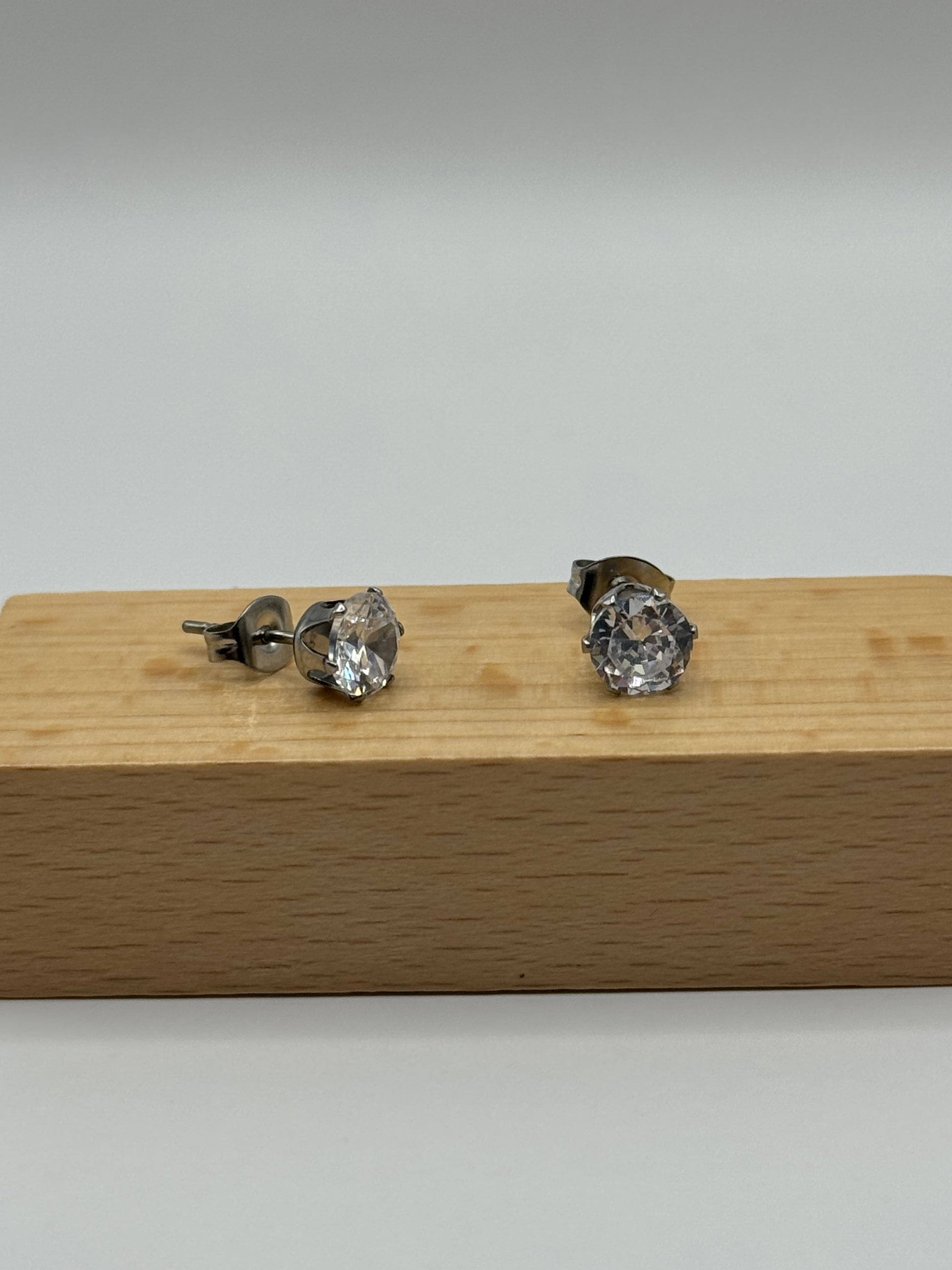 Silver cubic zirconia stud earrings shown from a side angle on a wooden block, The Ari Studs by EMPIECE™.