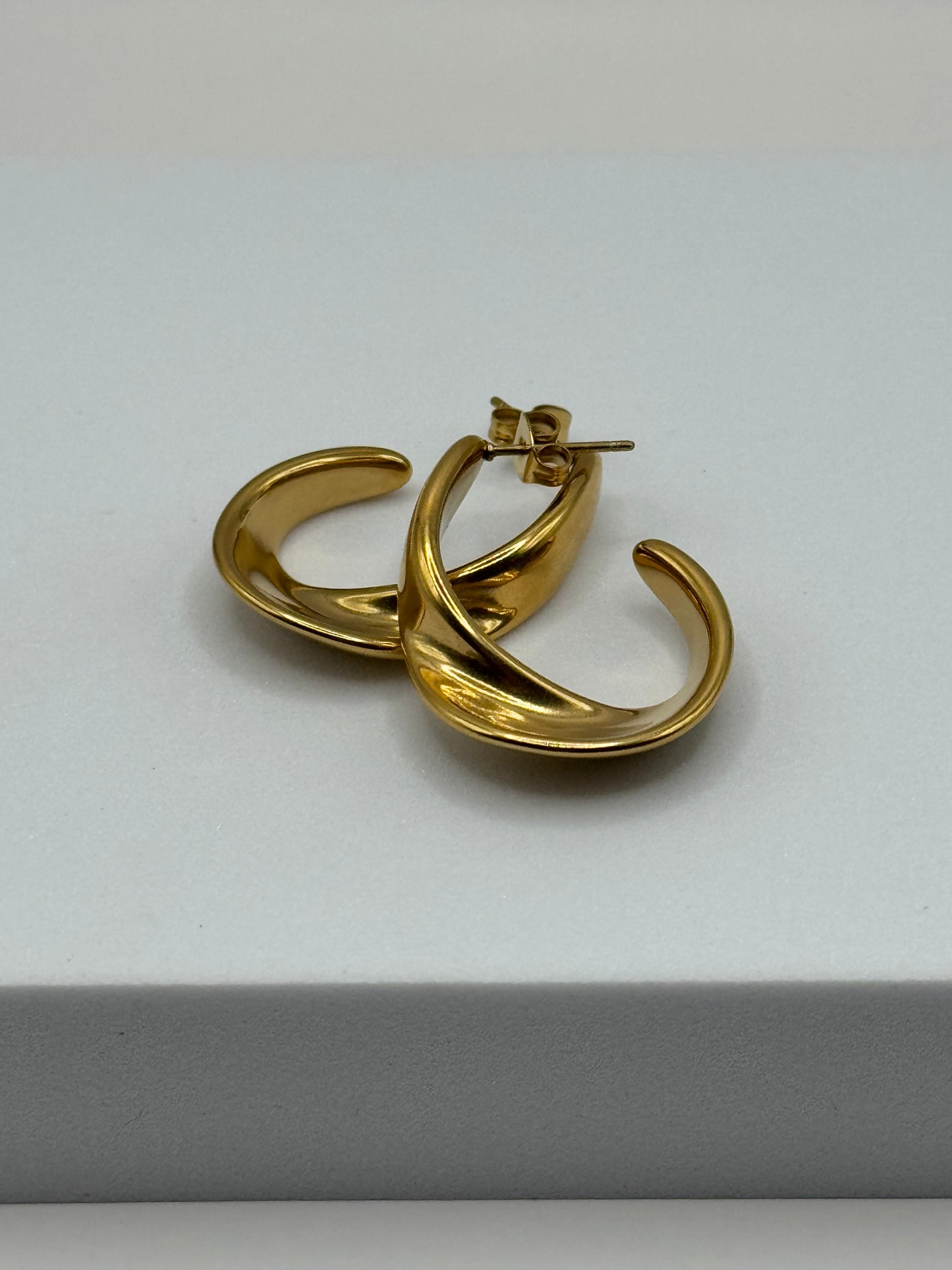 Angled view of gold sculptural C-shaped hoop stud earrings showing curved profile and polished finish, The Virelle Earrings by EMPIECE™.