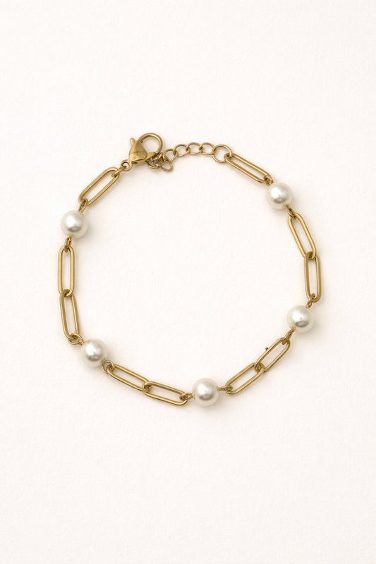Gold paperclip chain bracelet with station pearls on a white background